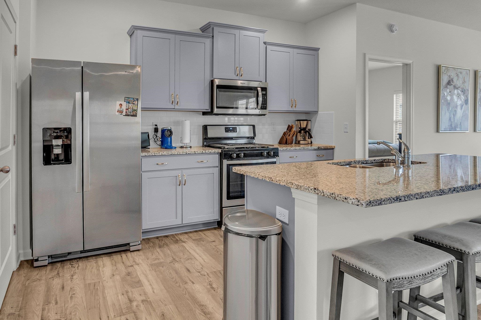 The kitchen offers light wood-style flooring, stainless steel-finished appliances, a modern sink, a breakfast bar, and a stylish backsplash for a polished look.