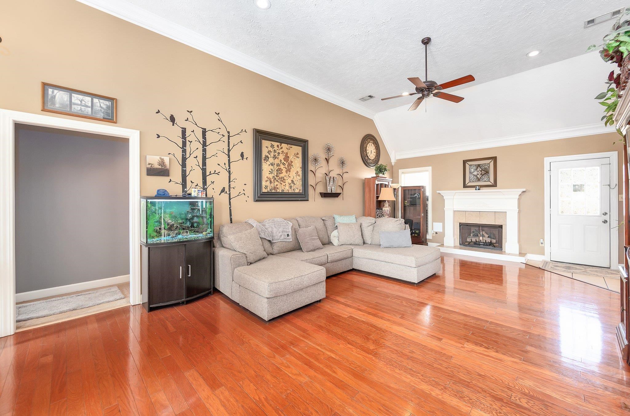 Living room featuring a fireplace, hardwood / wood-style floors, ornamental molding, ceiling fan, and vaulted ceiling