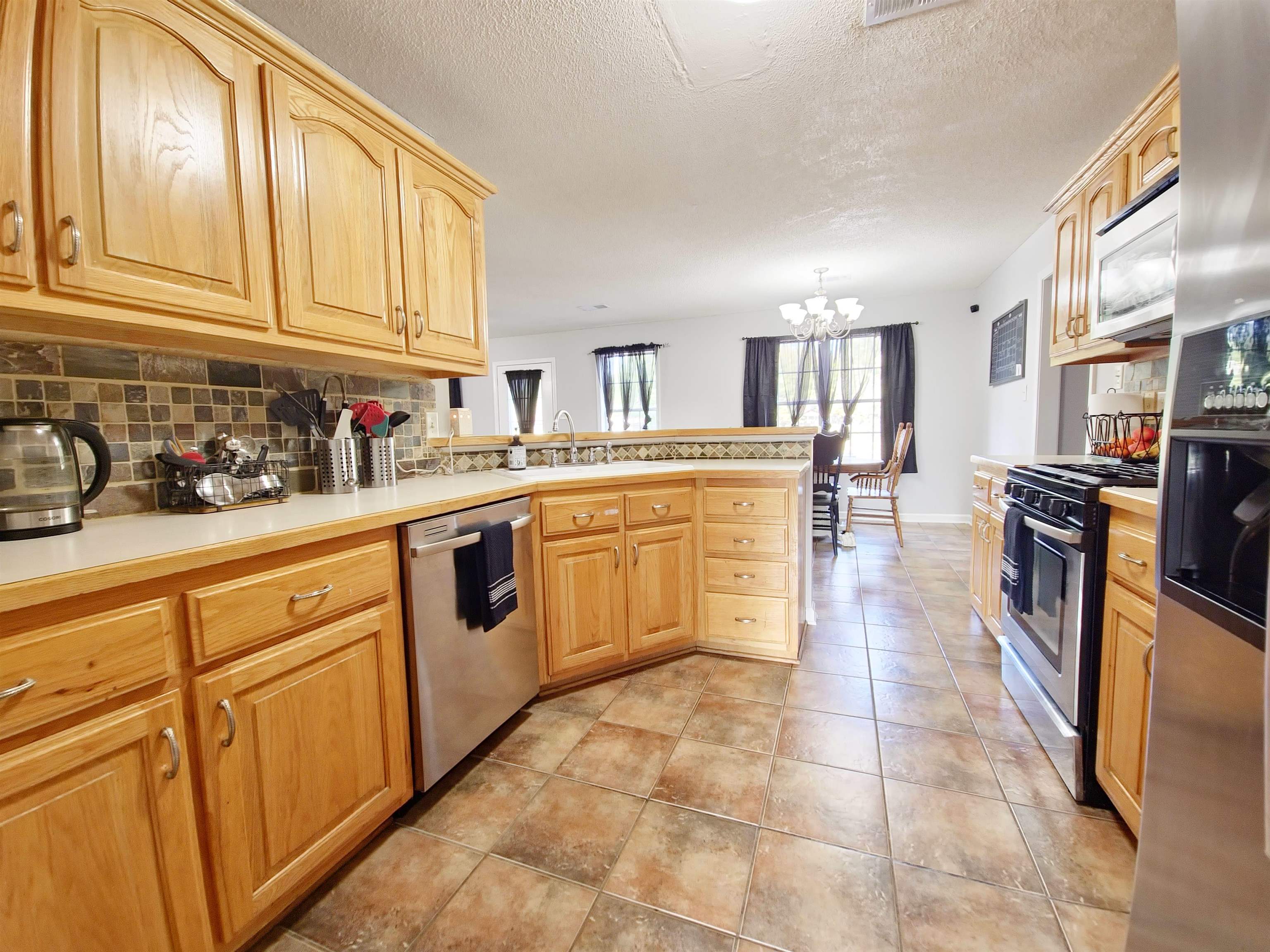 Kitchen with light tile patterned floors, tasteful backsplash, stainless steel appliances, kitchen peninsula, and a chandelier