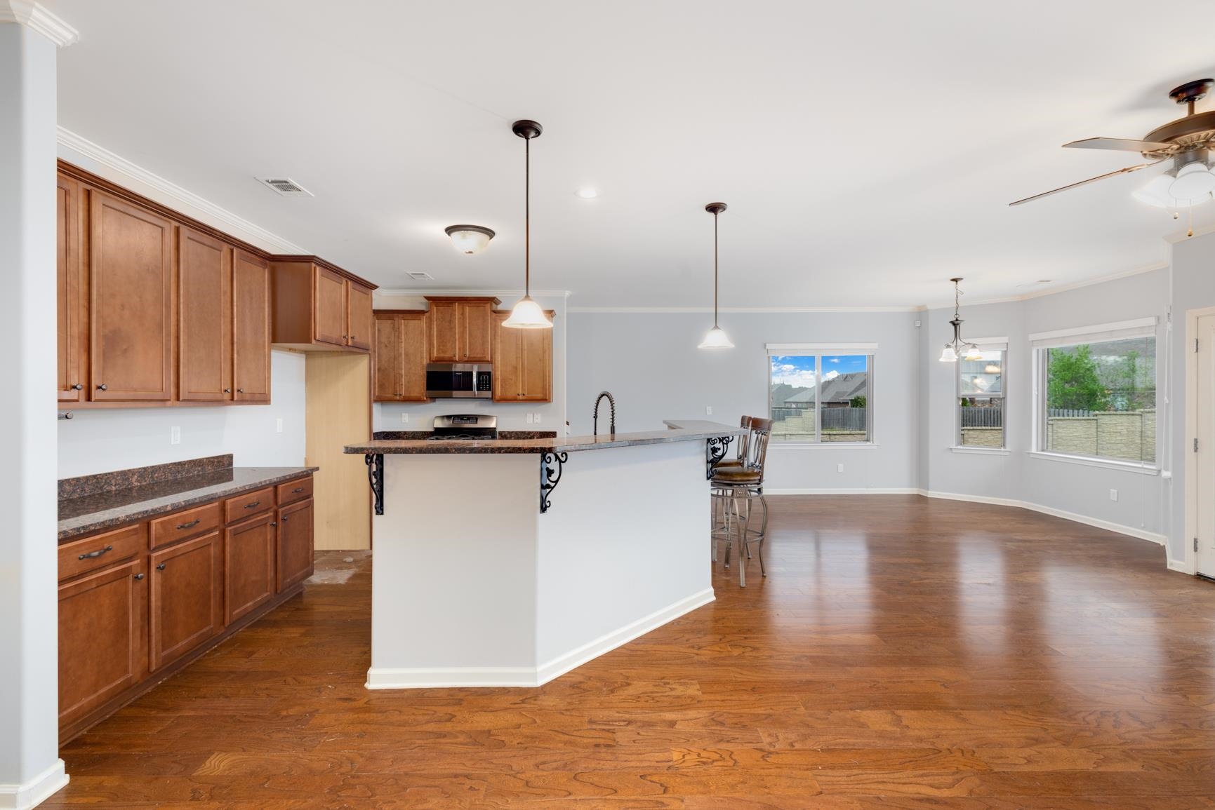 Kitchen featuring dark hardwood / wood-style floors, decorative light fixtures, appliances with stainless steel finishes, a kitchen bar, and ceiling fan