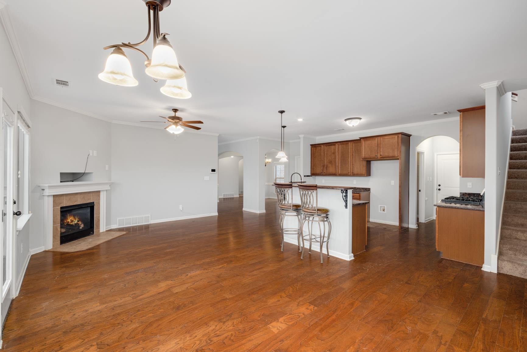 Kitchen featuring a fireplace, ceiling fan with notable chandelier, ornamental molding, hanging light fixtures, and dark hardwood / wood-style floors