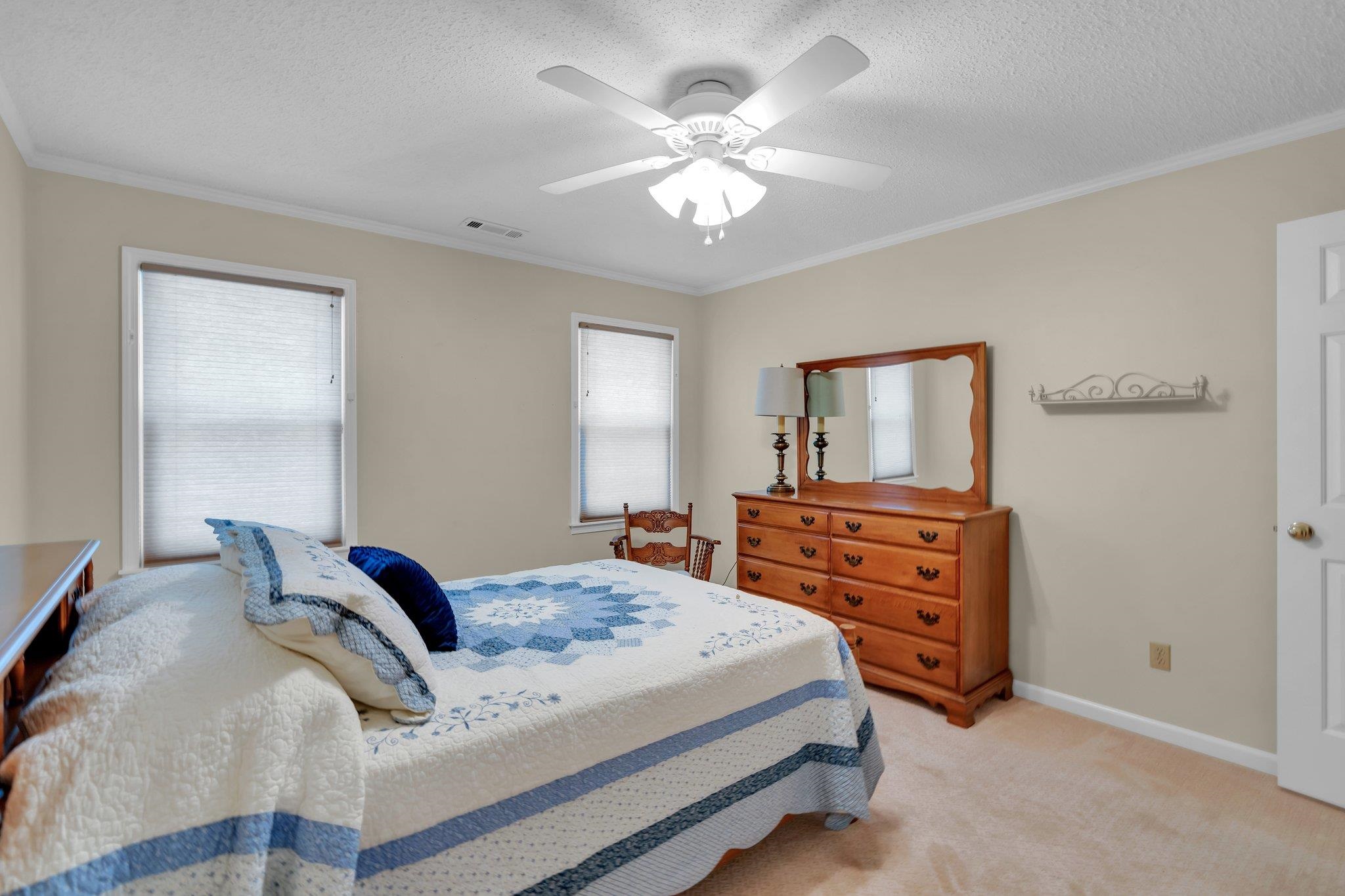 Carpeted bedroom with a textured ceiling, ceiling fan, and ornamental molding