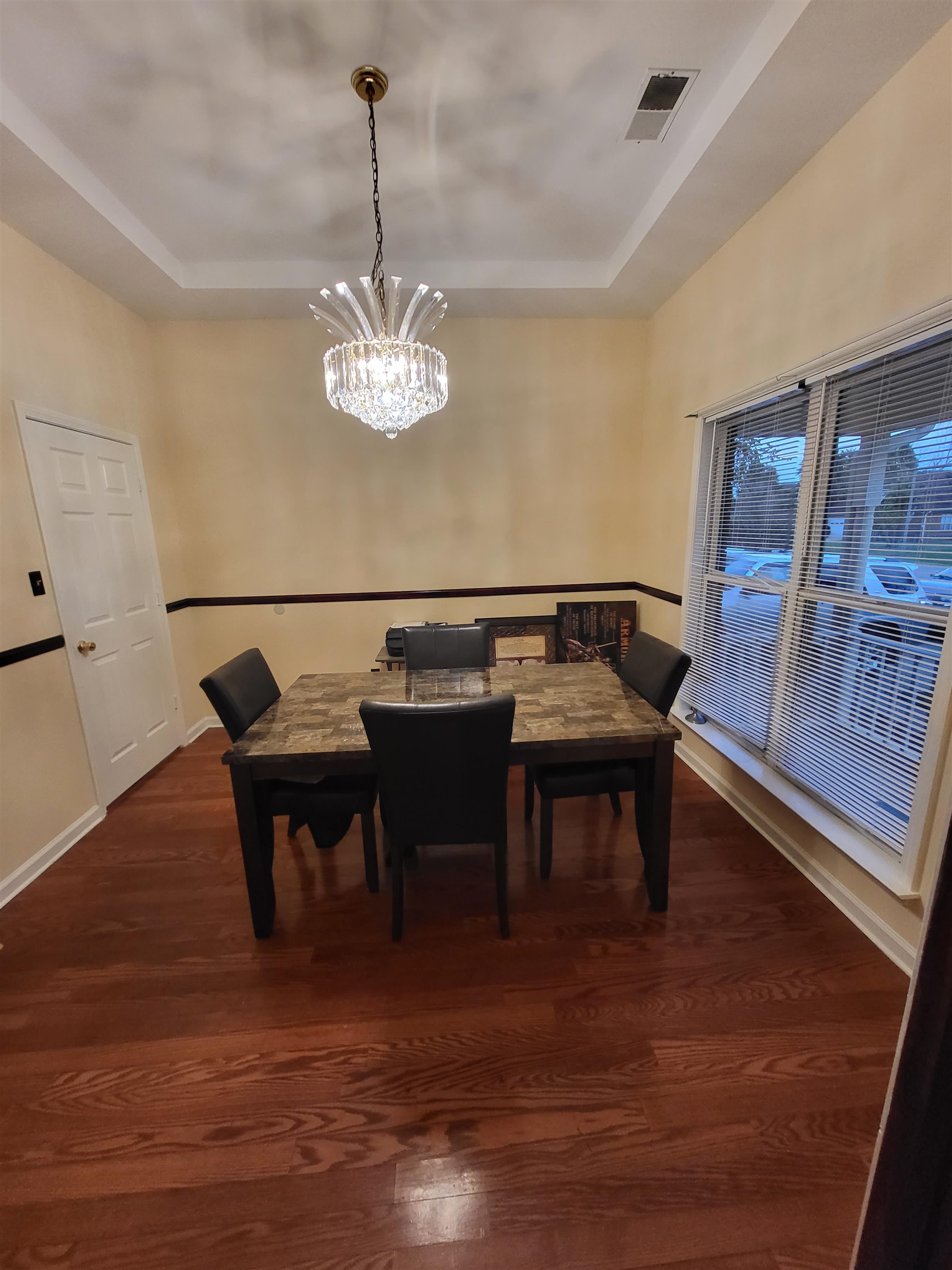 Dining room featuring dark wood-type flooring, a chandelier, and a raised ceiling