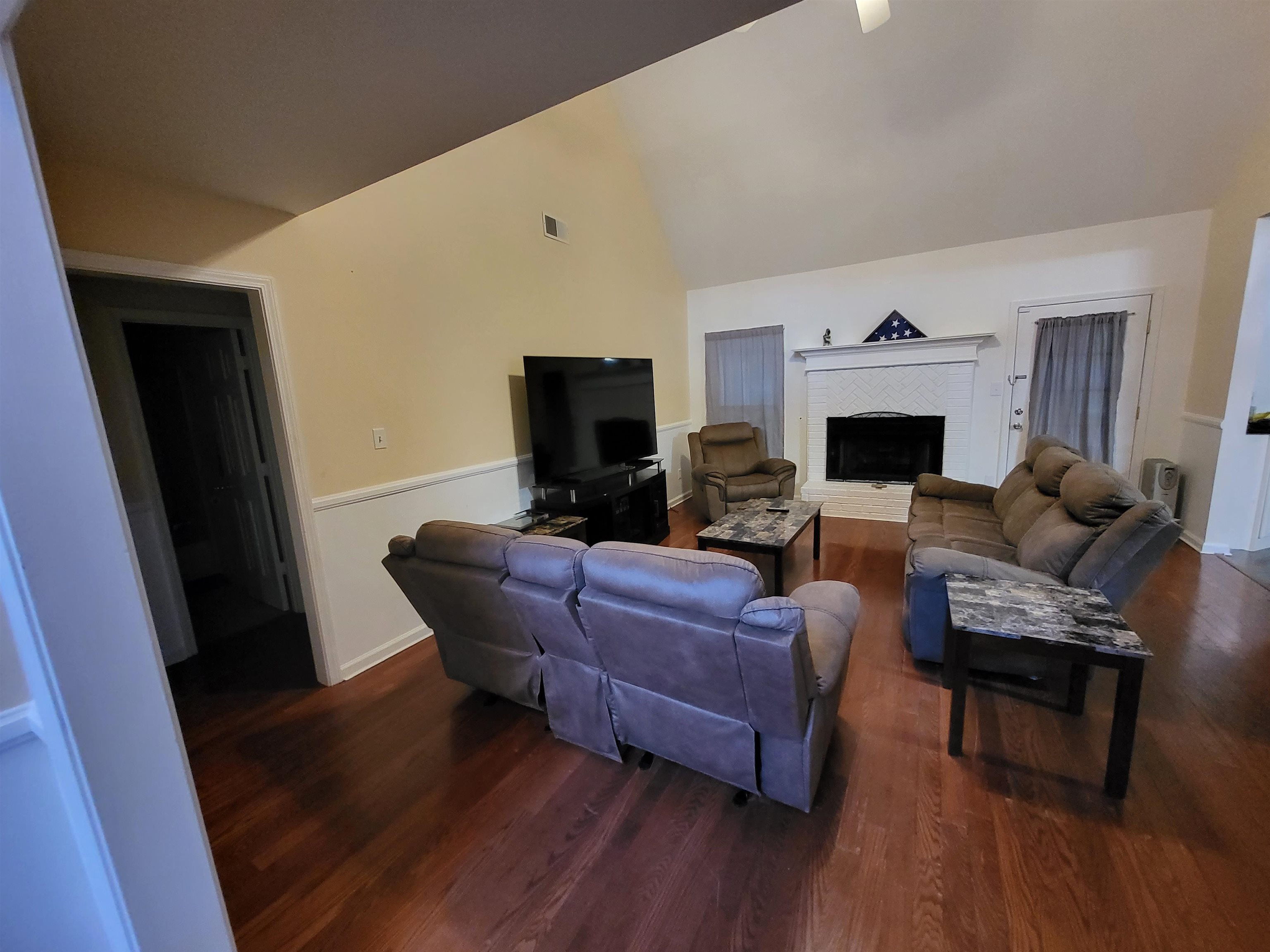 Living room featuring vaulted ceiling, dark hardwood / wood-style flooring, and a brick fireplace