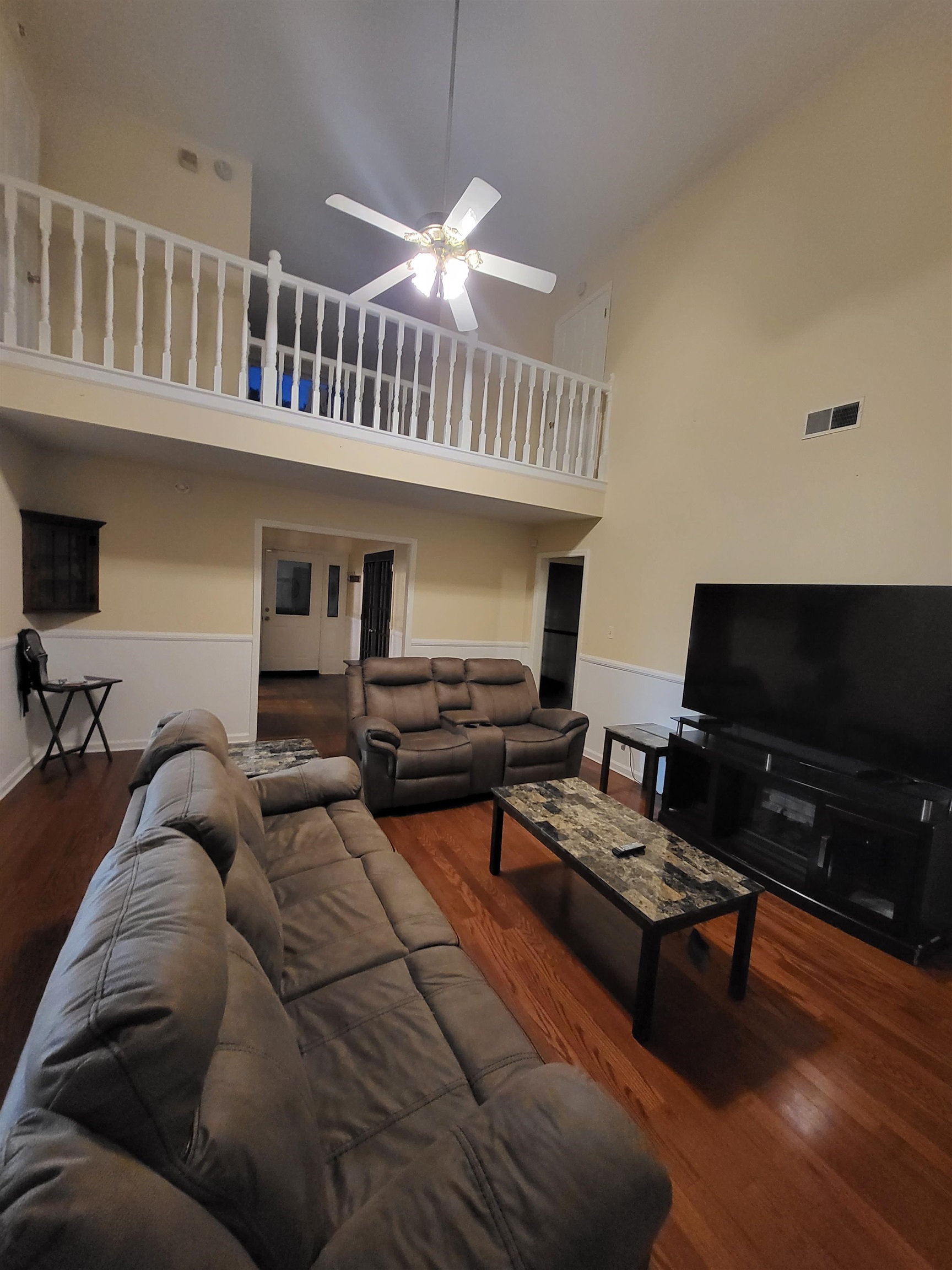 Living room featuring hardwood / wood-style floors, ceiling fan, and a towering ceiling