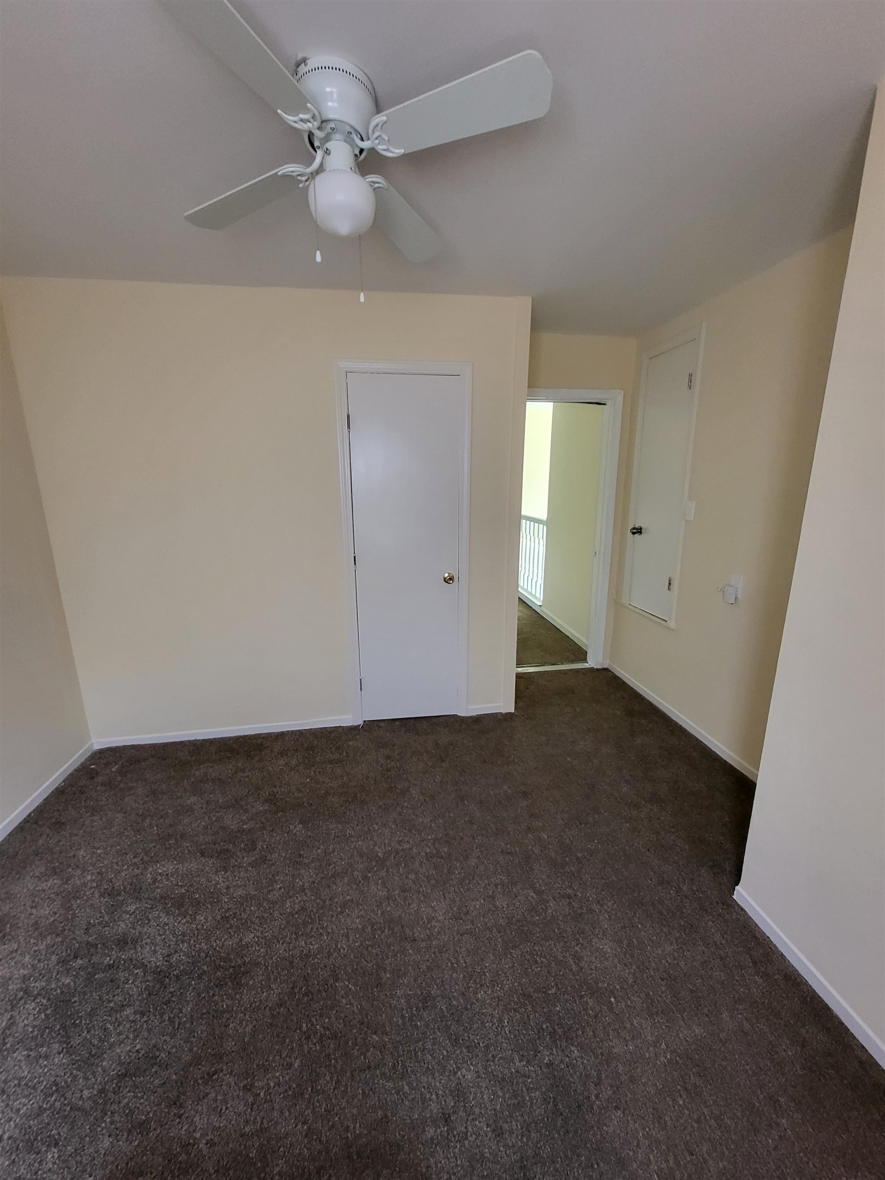 Empty room featuring ceiling fan and dark colored carpet