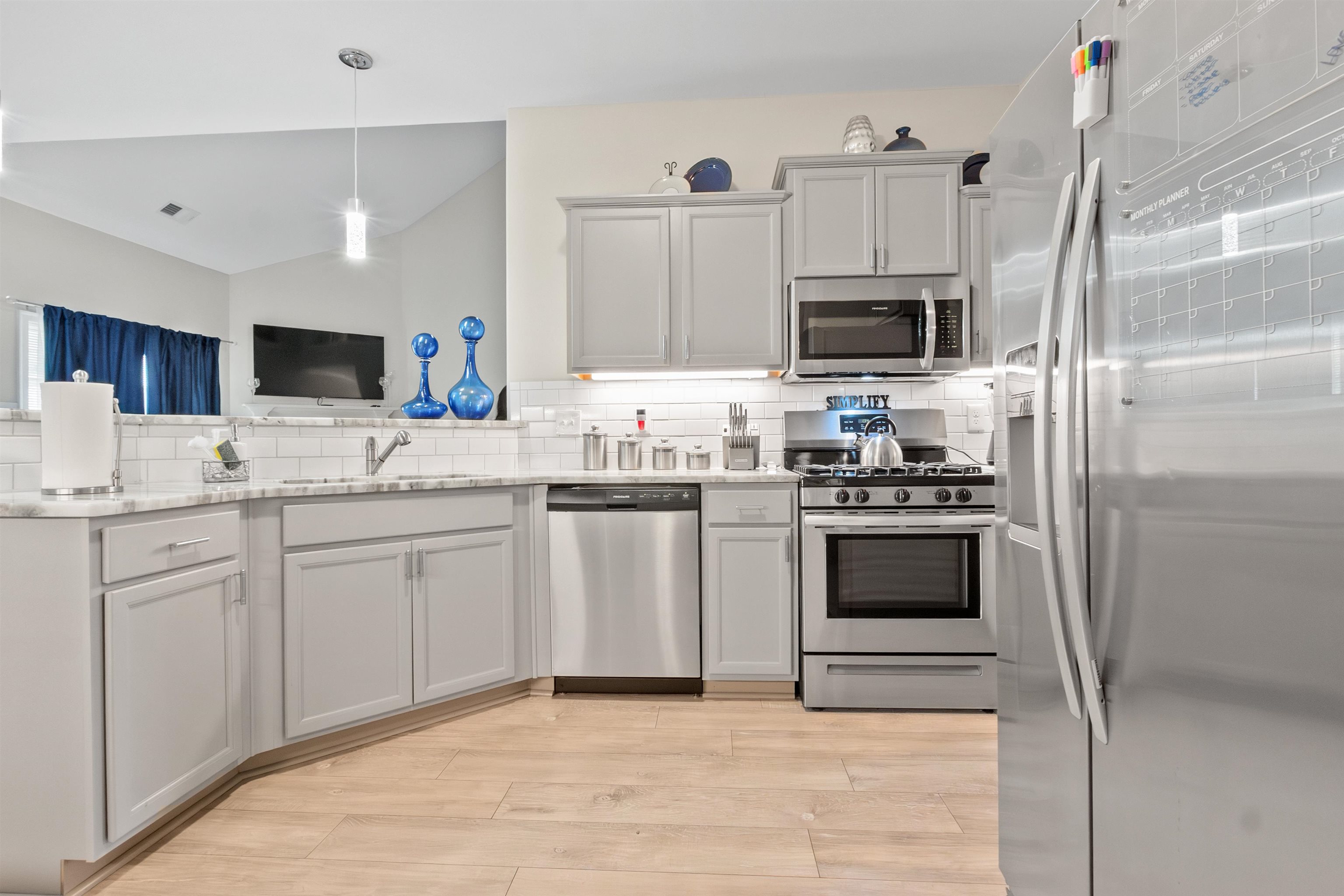 Kitchen featuring light stone countertops, light hardwood / wood-style flooring, backsplash, appliances with stainless steel finishes, and sink