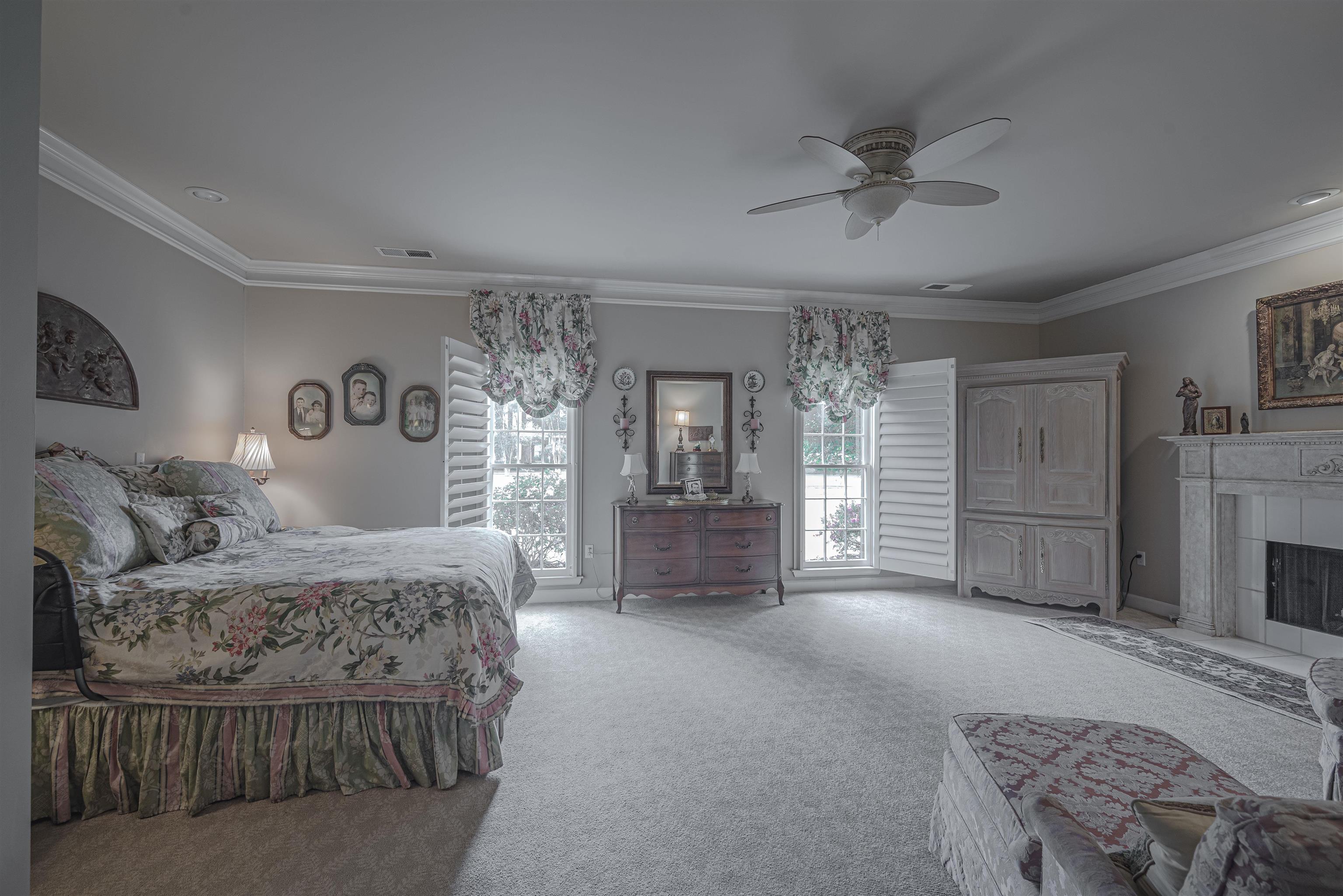 Carpeted bedroom featuring crown molding, ceiling fan, and a tiled fireplace