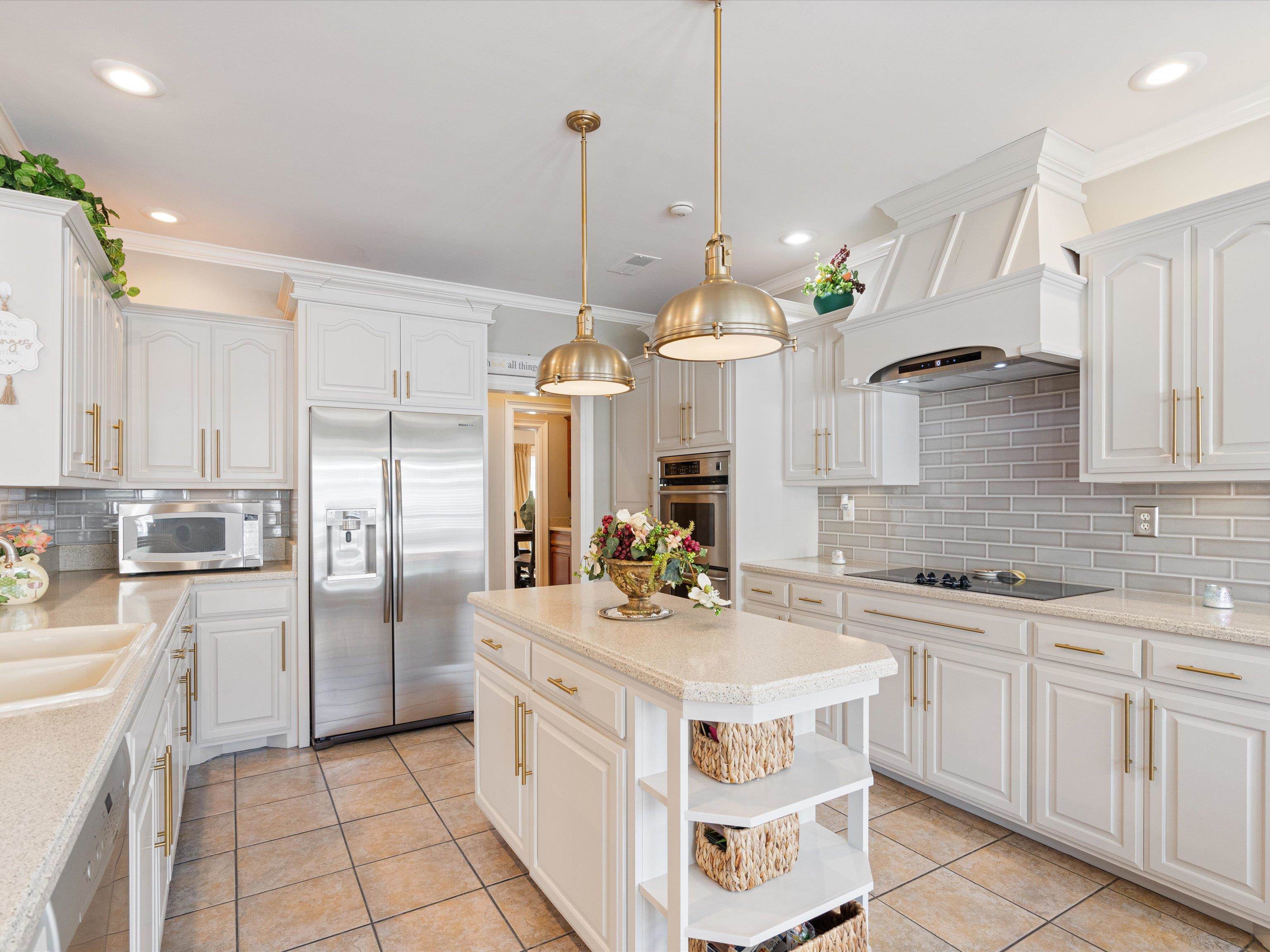 Kitchen featuring light tile patterned floors, backsplash, premium range hood, appliances with stainless steel finishes, and decorative light fixtures