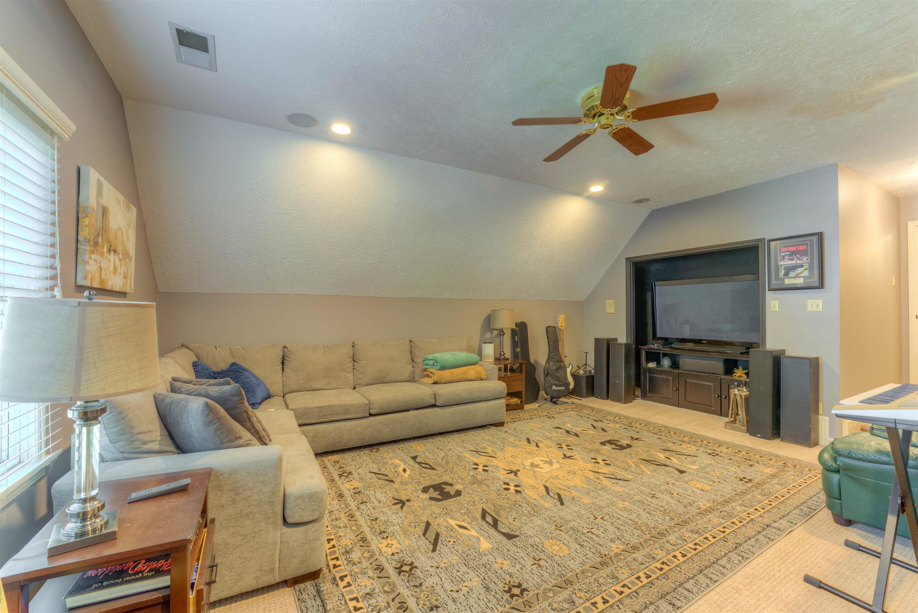 Living room with ceiling fan, a textured ceiling, lofted ceiling, and carpet flooring