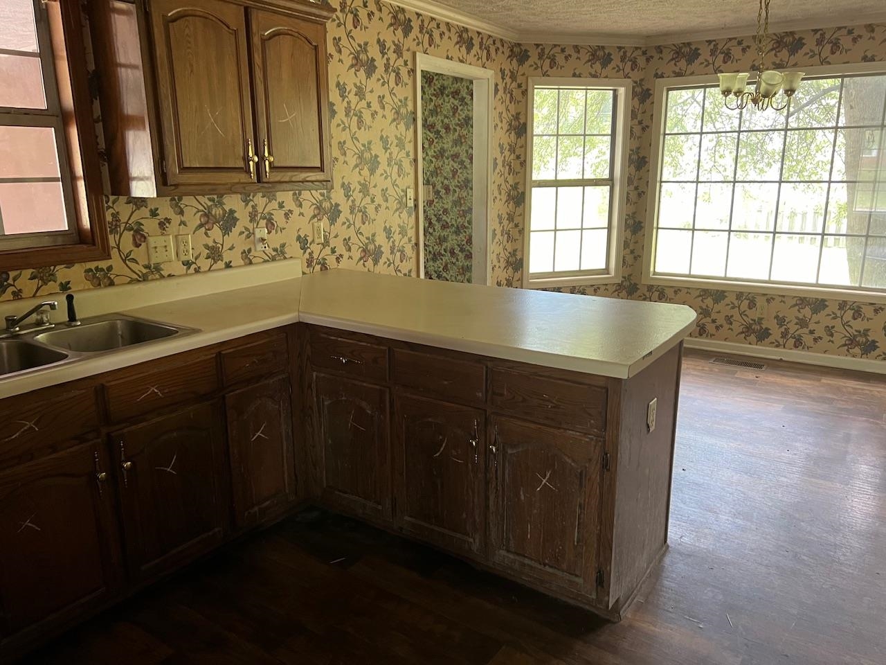 Kitchen featuring hanging light fixtures, dark wood-type flooring, kitchen peninsula, sink, and a chandelier