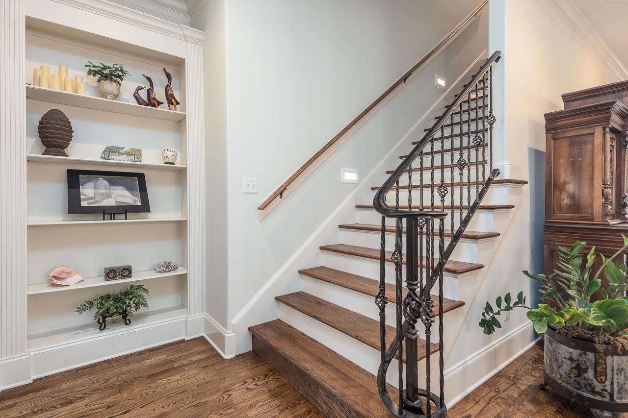 Stairs with wood-type flooring, built in shelves, and crown molding