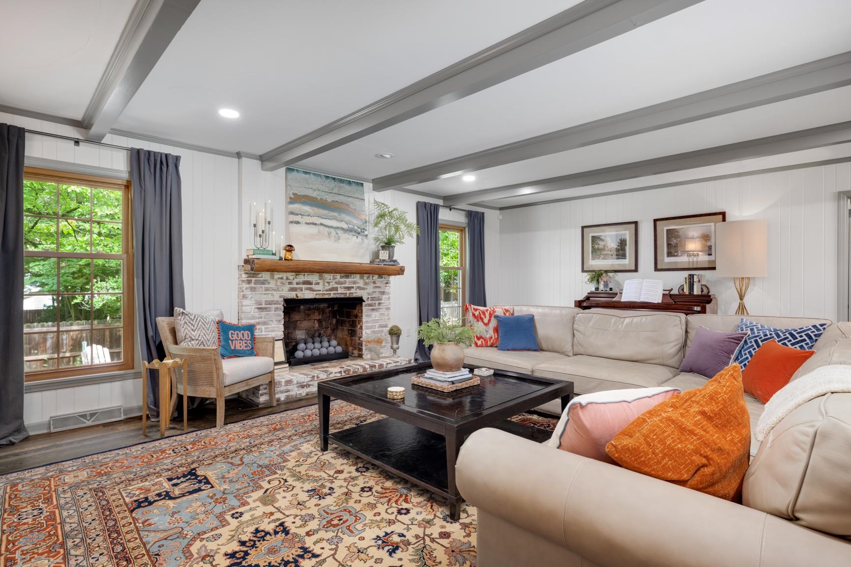 Living room with a brick fireplace, a wealth of natural light, beamed ceiling, and hardwood / wood-style floors