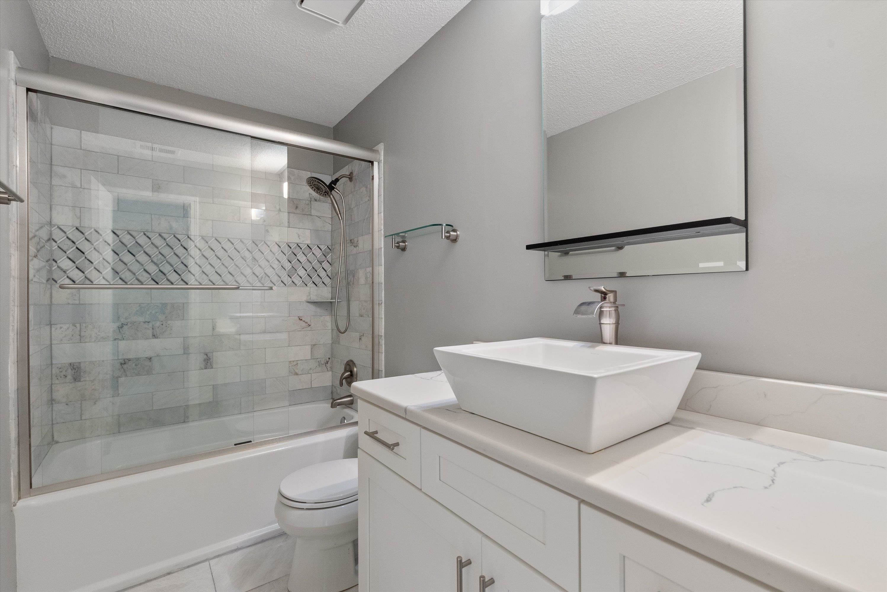 Full bathroom with tile patterned flooring, a textured ceiling, bath / shower combo with glass door, vanity, and toilet