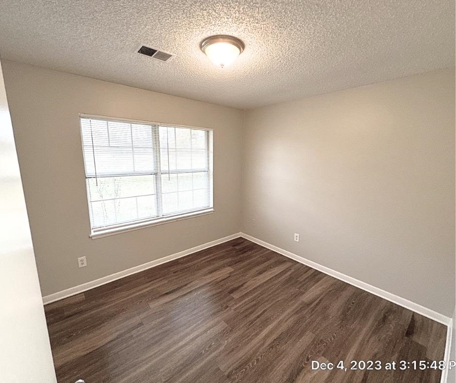 Empty room featuring a textured ceiling and dark hardwood / wood-style flooring