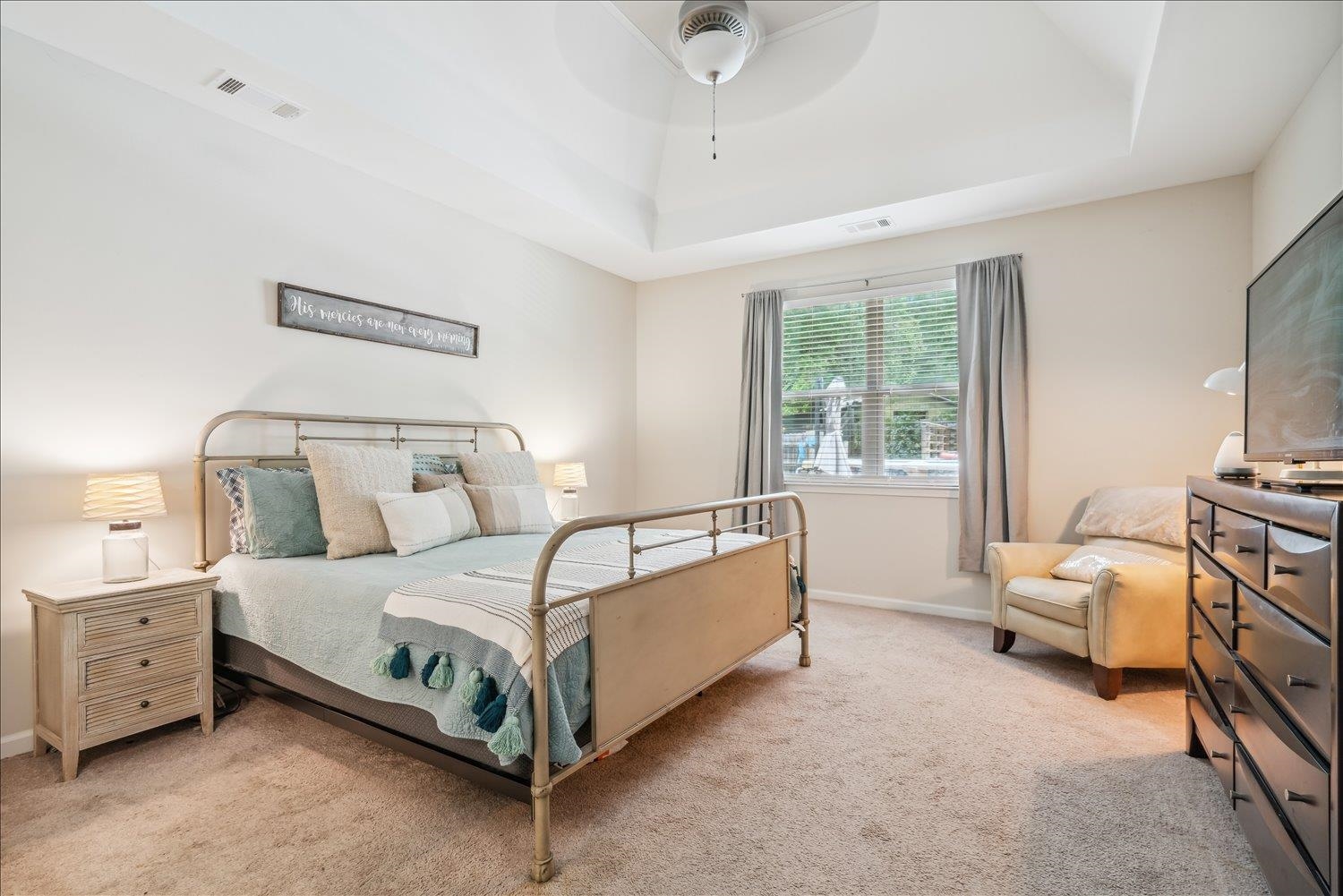 Carpeted bedroom with a tray ceiling and ceiling fan