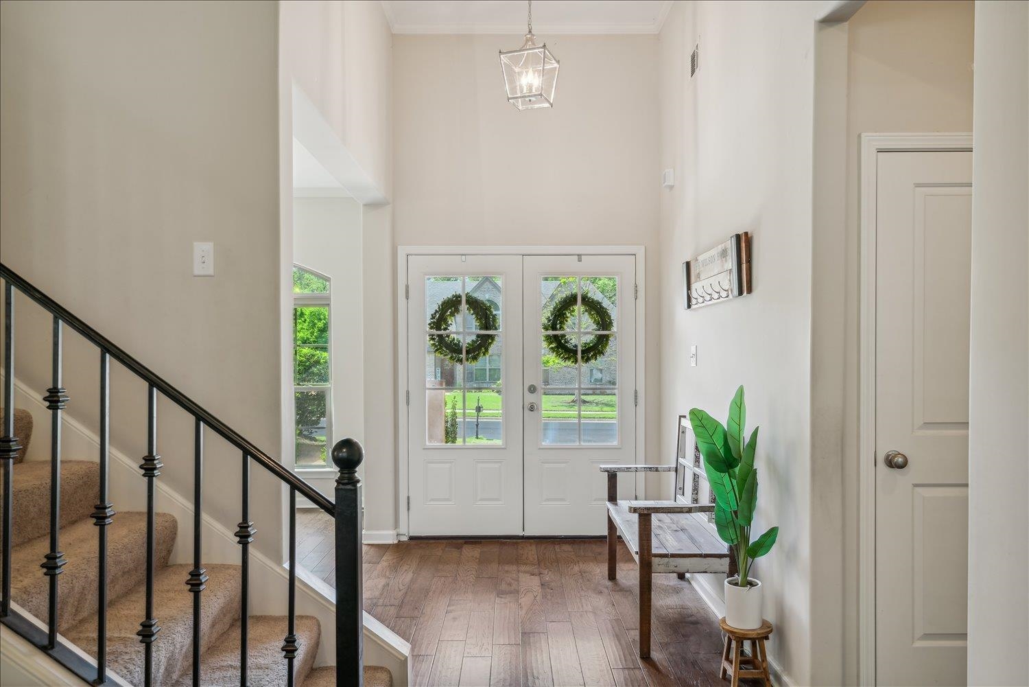 Foyer featuring a towering ceiling, wood-type flooring, french doors, ornamental molding, and a chandelier