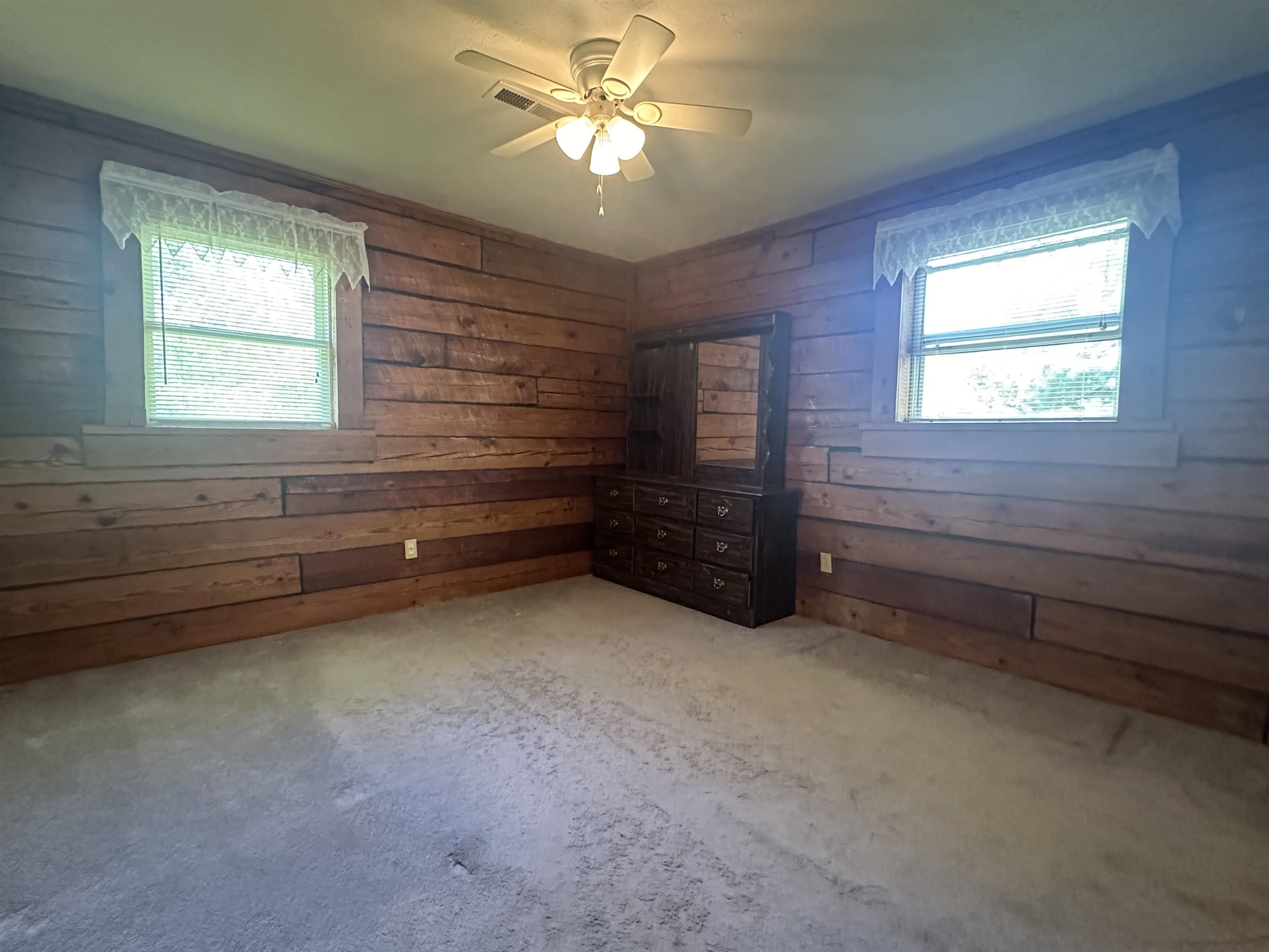 Carpeted spare room with wooden walls, ceiling fan, and plenty of natural light