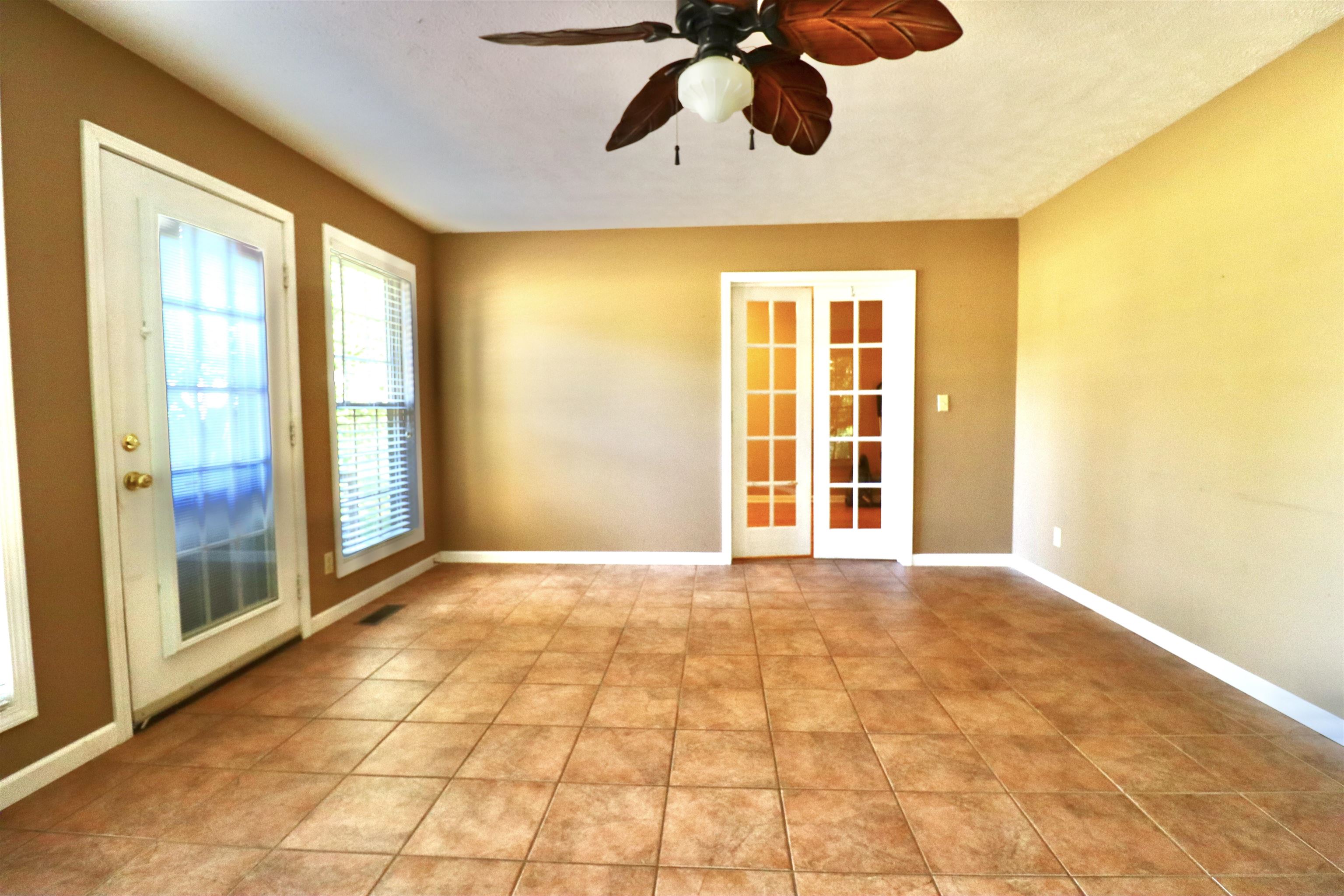 Tiled spare room featuring ceiling fan and french doors