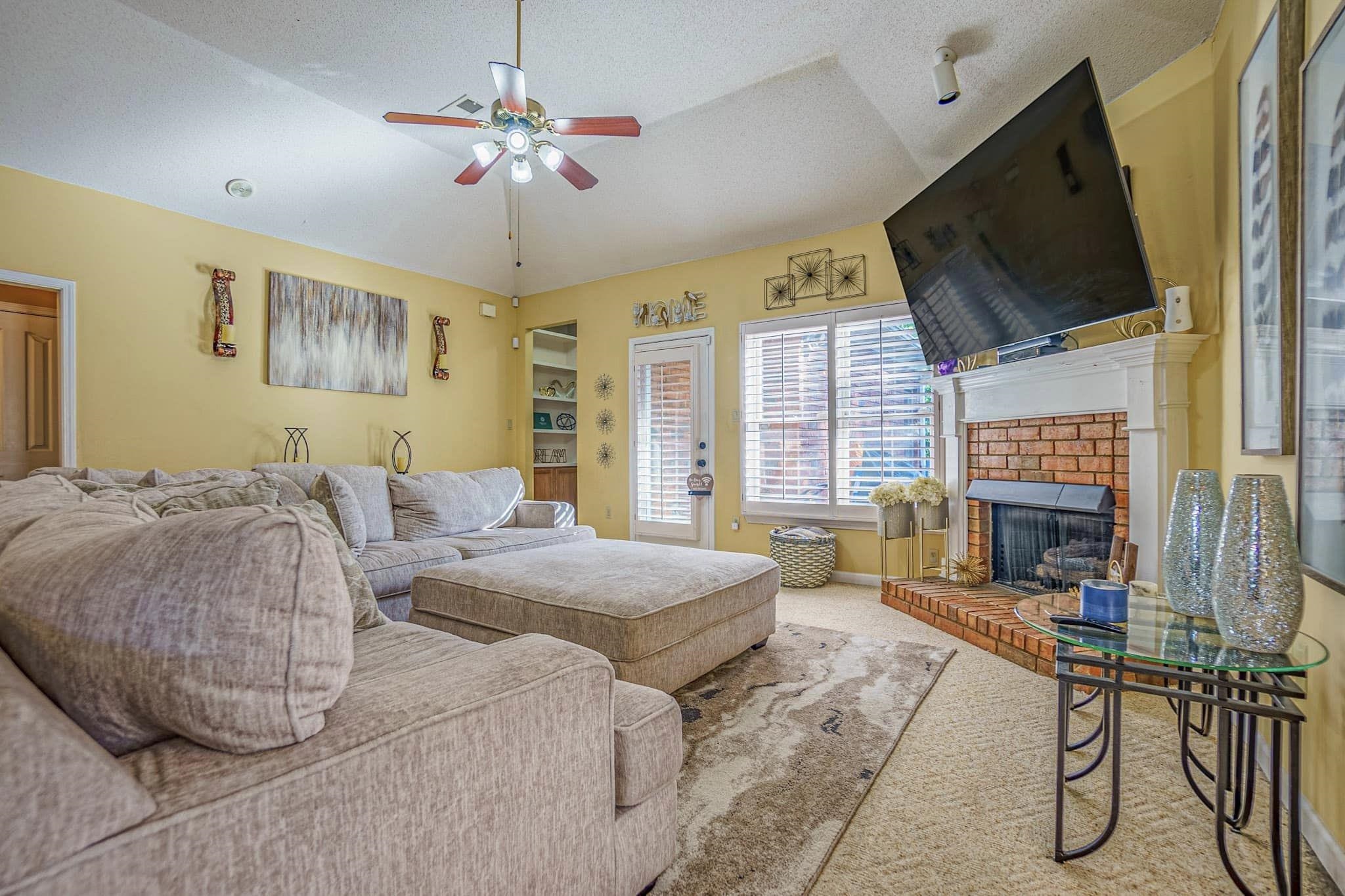 Living room with a textured ceiling, lofted ceiling, carpet floors, a brick fireplace, and ceiling fan