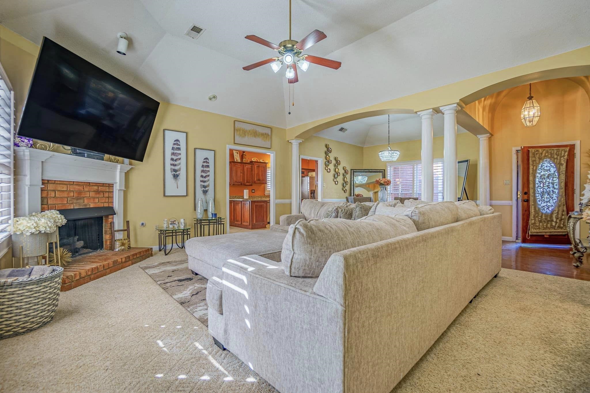 Living room with wood-type flooring, ceiling fan with notable chandelier, lofted ceiling, a fireplace, and ornate columns