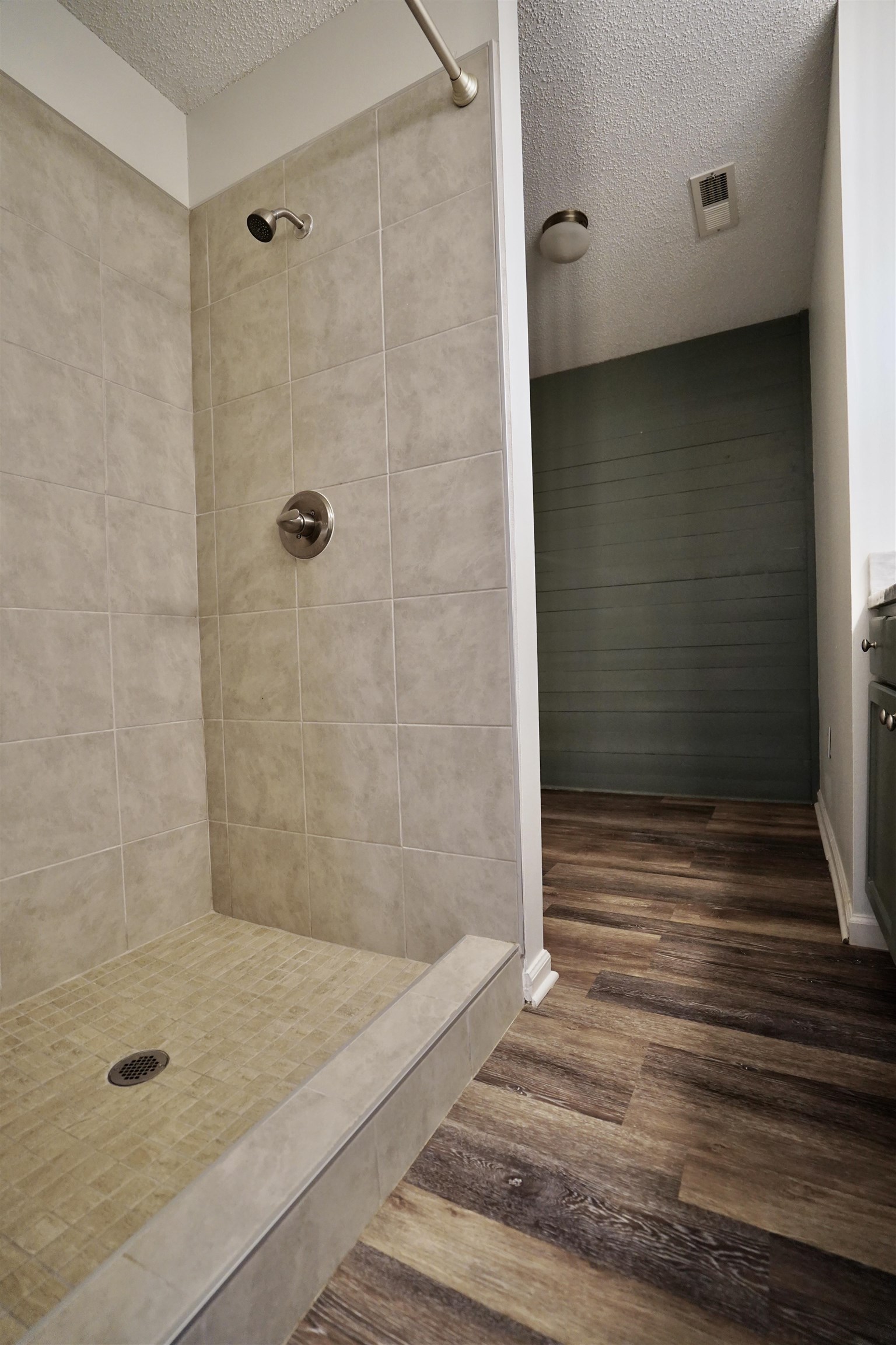 Bathroom with a tile shower, a textured ceiling, and hardwood / wood-style floors