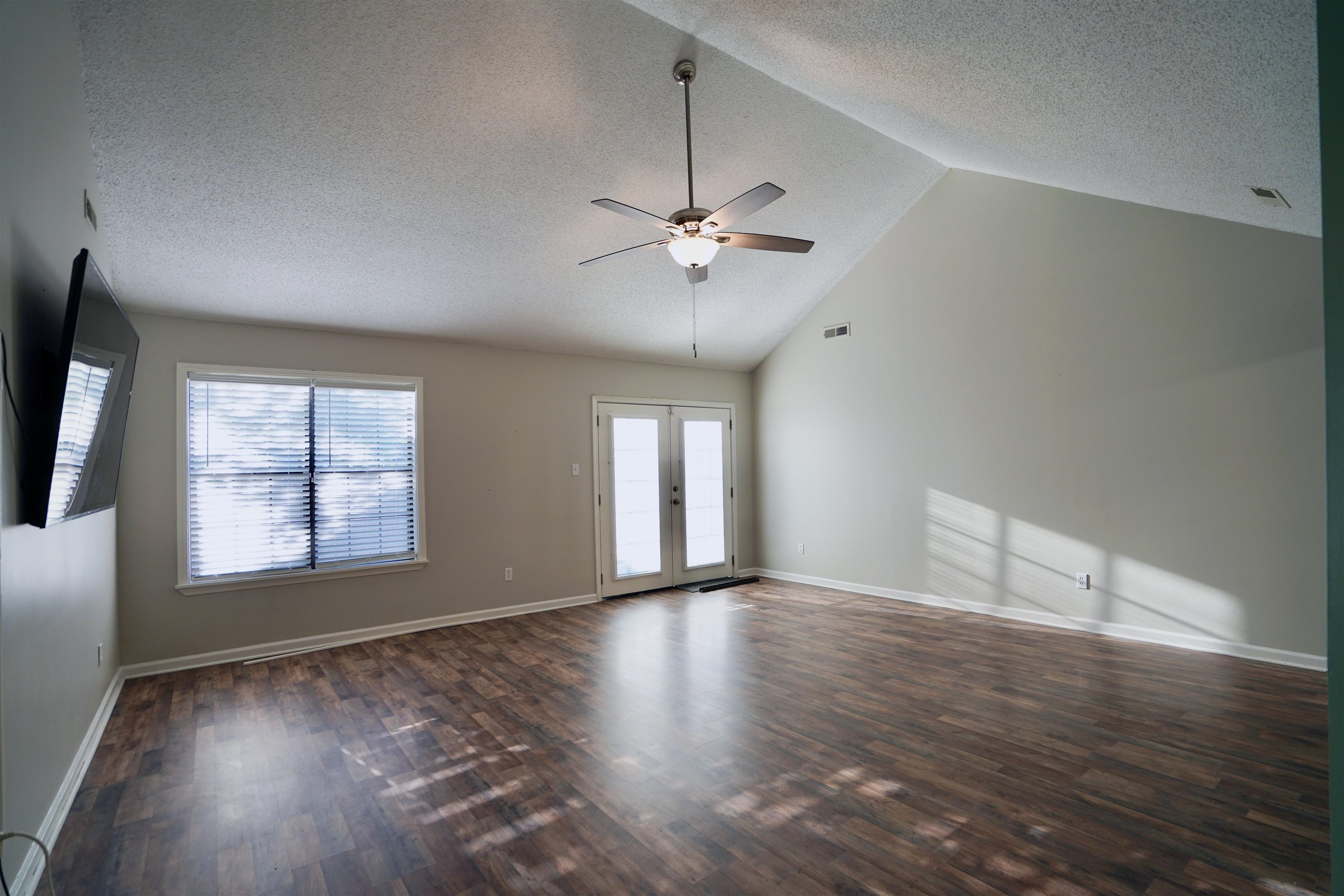 Spare room with a textured ceiling, lofted ceiling, dark wood-type flooring, and ceiling fan