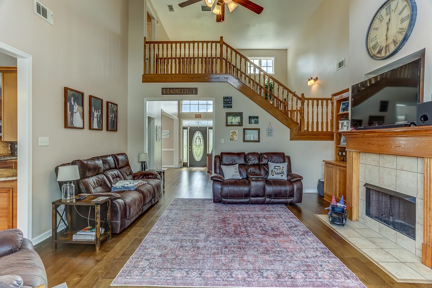 Living room with ceiling fan, hardwood / wood-style flooring, a fireplace, and a towering ceiling