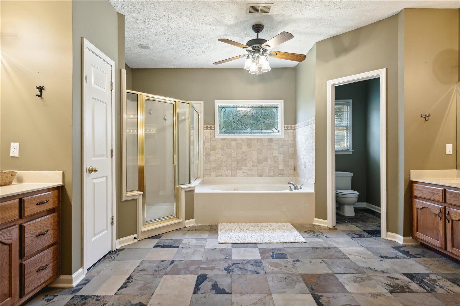 Full bathroom with vanity, a textured ceiling, independent shower and bath, ceiling fan, and toilet