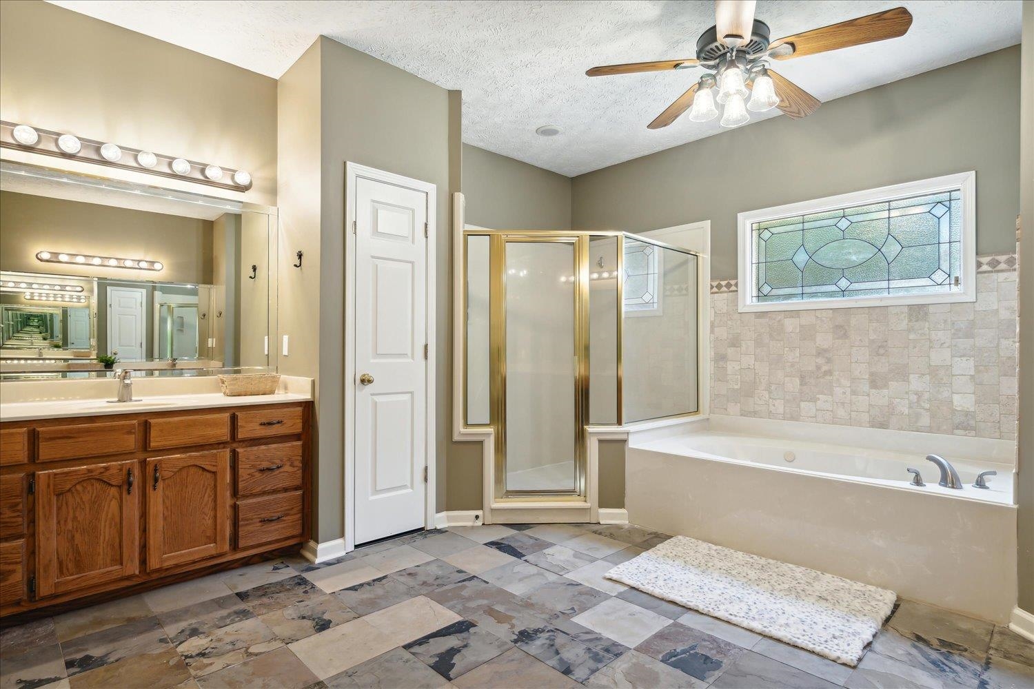 Bathroom with a textured ceiling, ceiling fan, vanity, and separate shower and tub