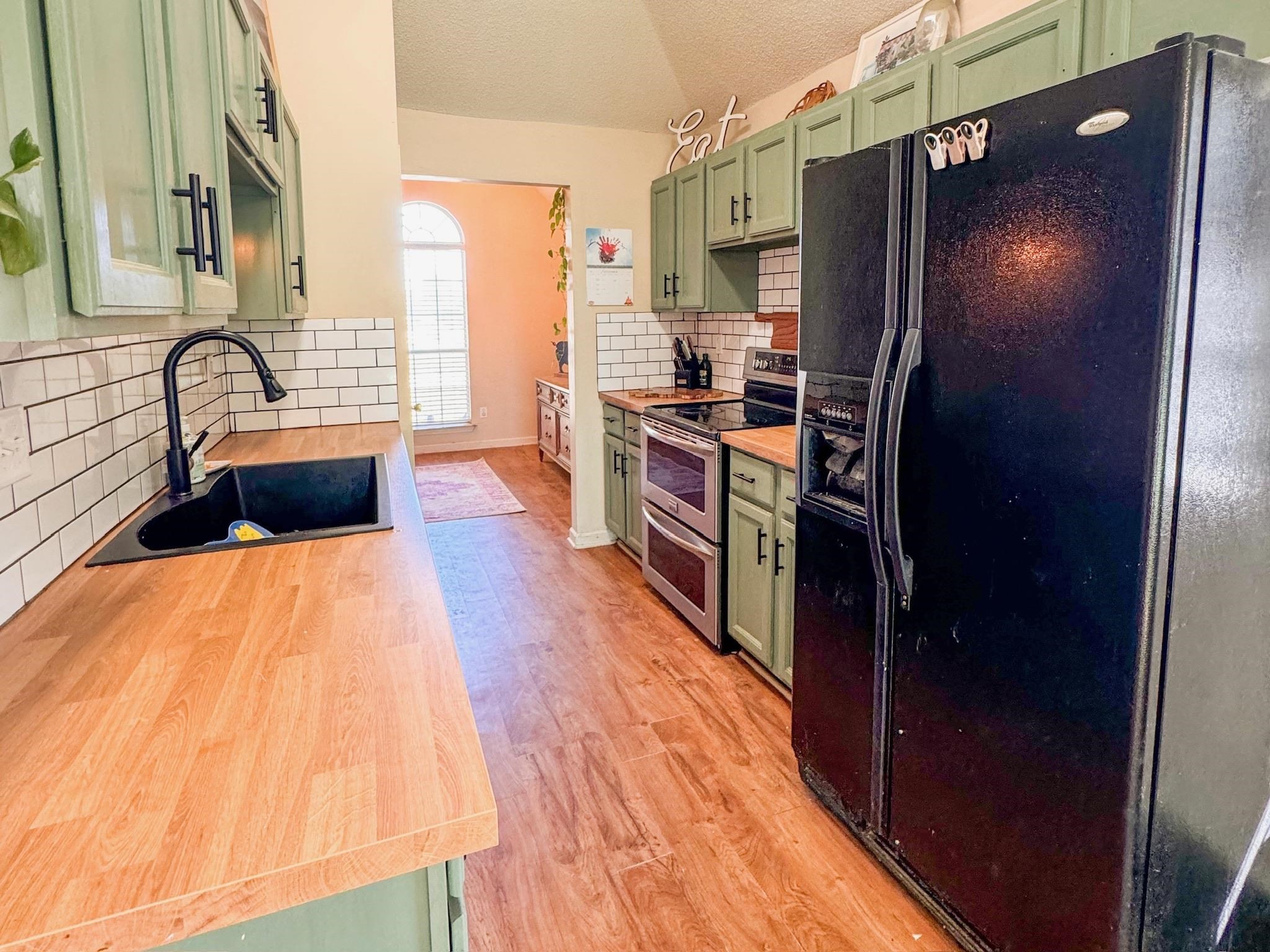 Kitchen with black fridge with ice dispenser, green cabinetry, range with two ovens, vaulted ceiling