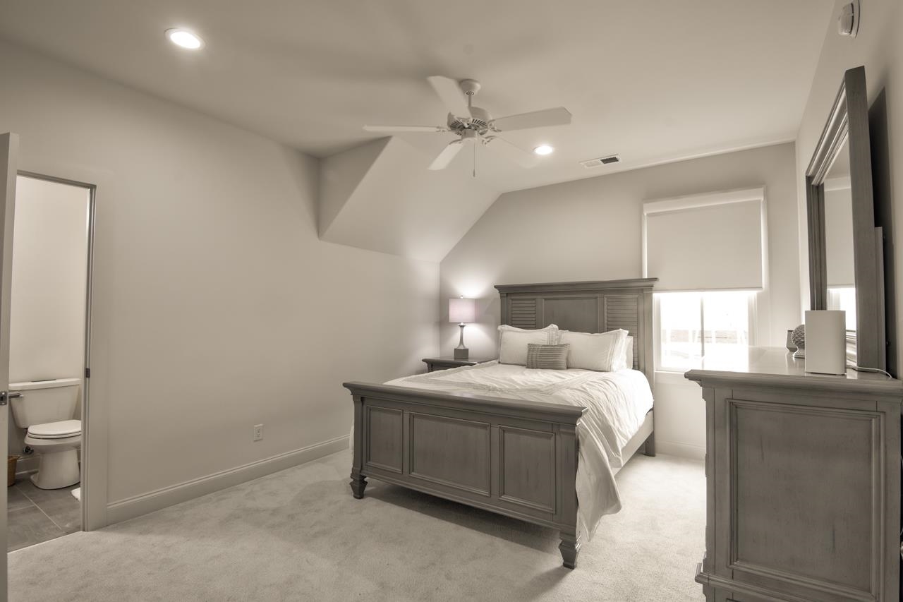 Carpeted bedroom with lofted ceiling, ensuite bath, and ceiling fan