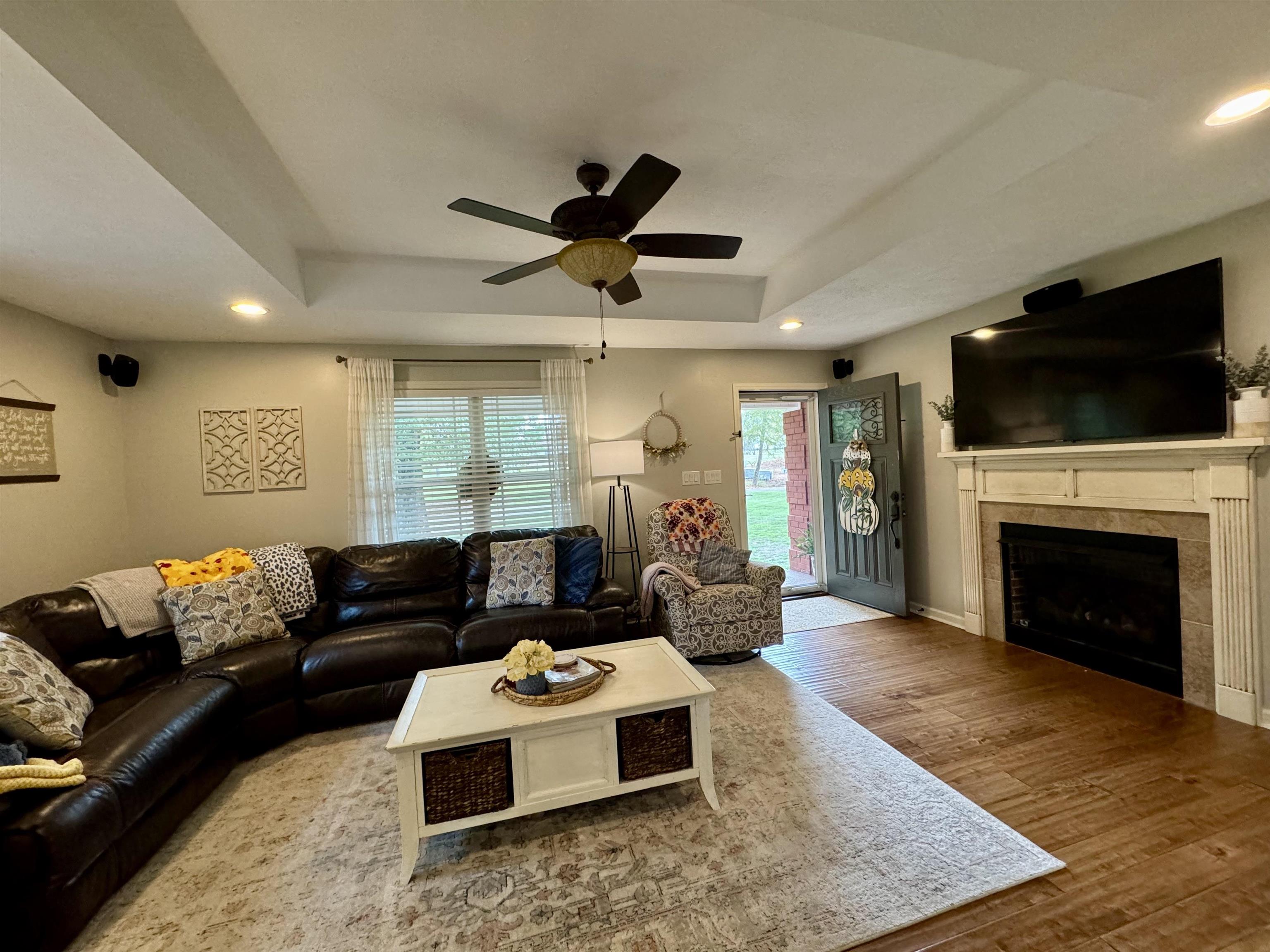Living room with wood-type flooring, a tray ceiling, ceiling fan, and plenty of natural light