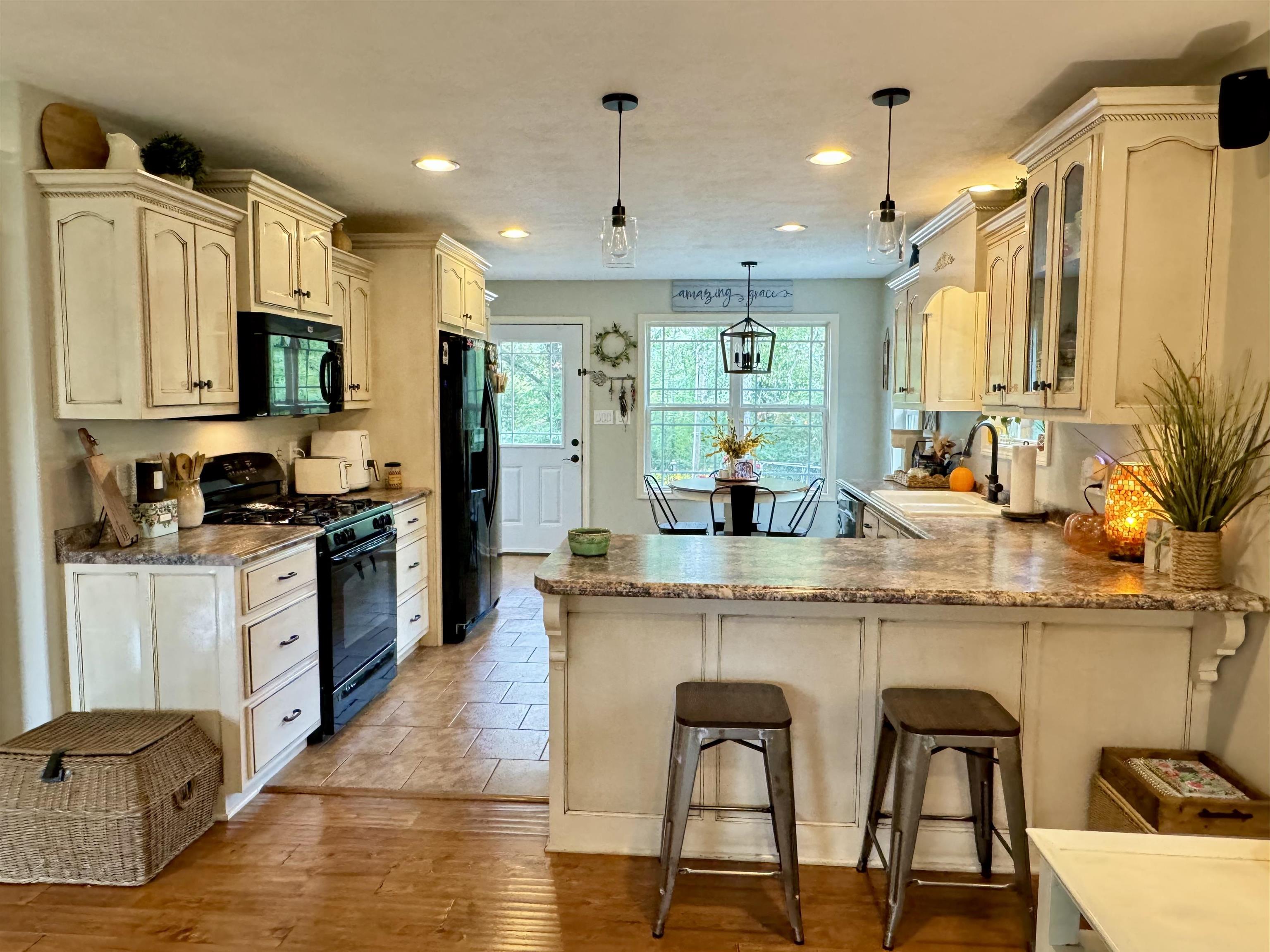 Kitchen with light hardwood / wood-style floors, pendant lighting, black appliances, a kitchen bar, and sink