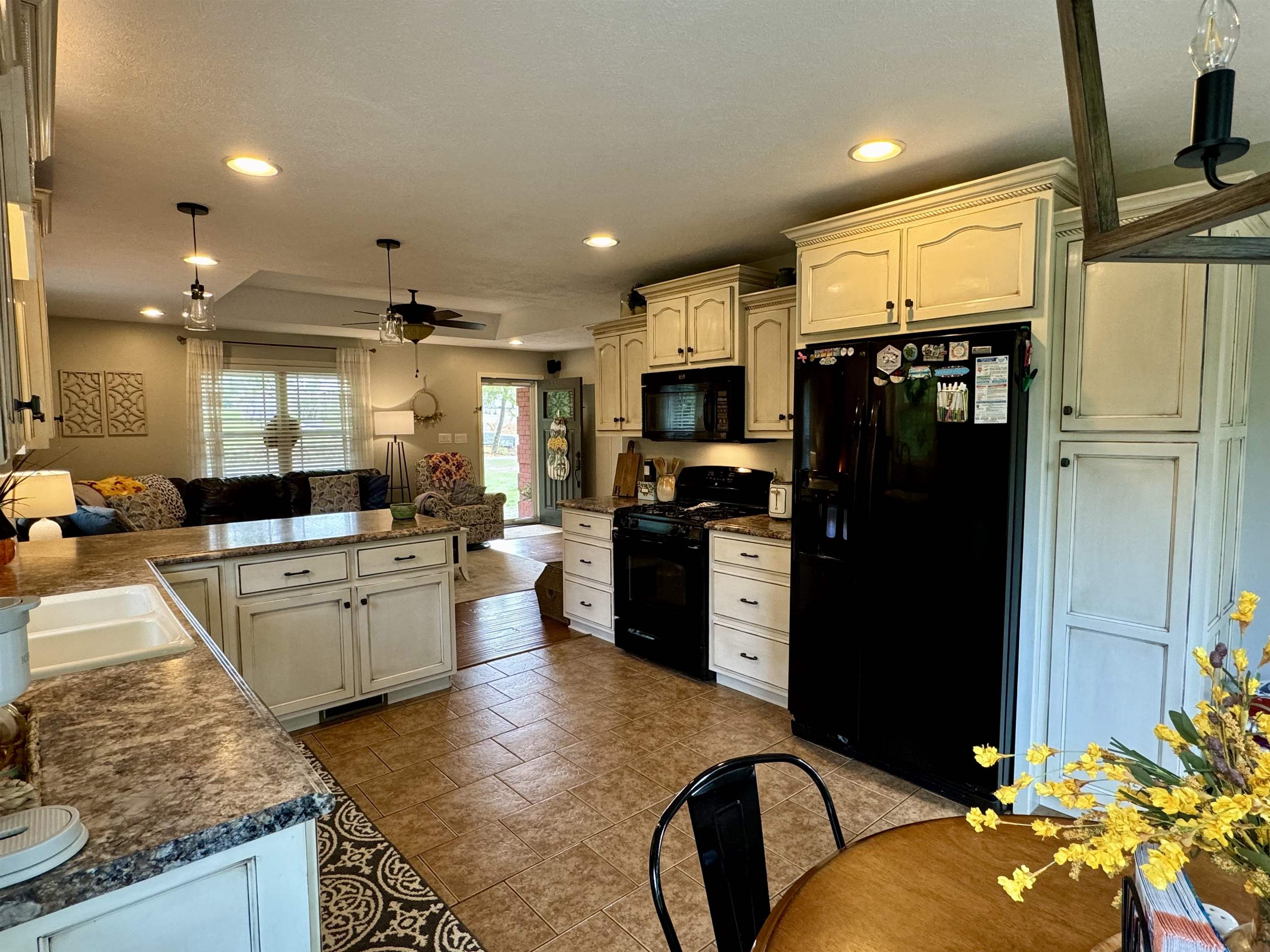 Kitchen with black appliances, ceiling fan, hanging light fixtures, and sink
