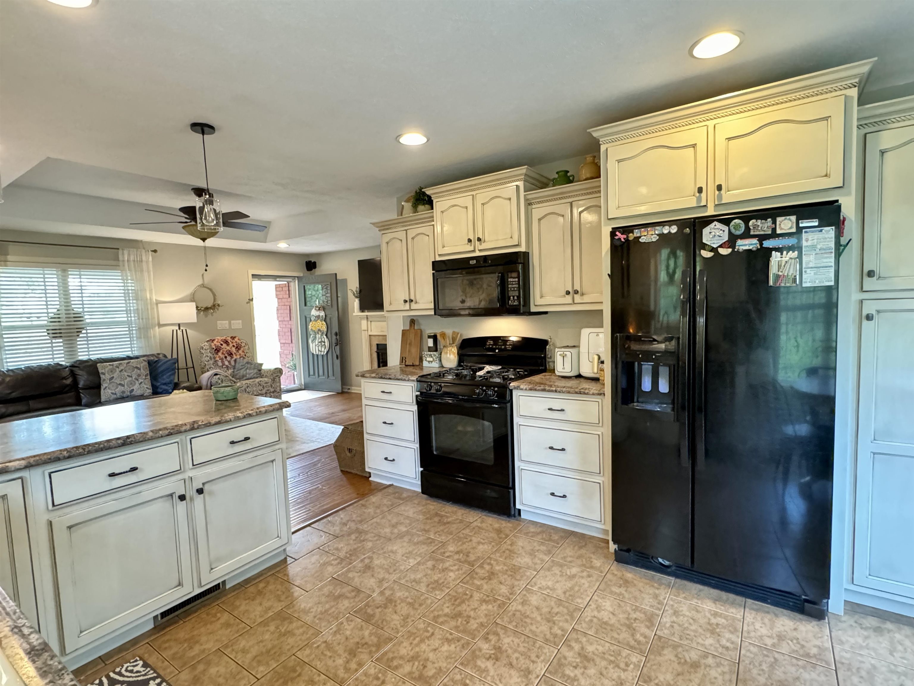 Kitchen with ceiling fan, cream cabinets, black appliances, a tray ceiling, and light wood-type flooring