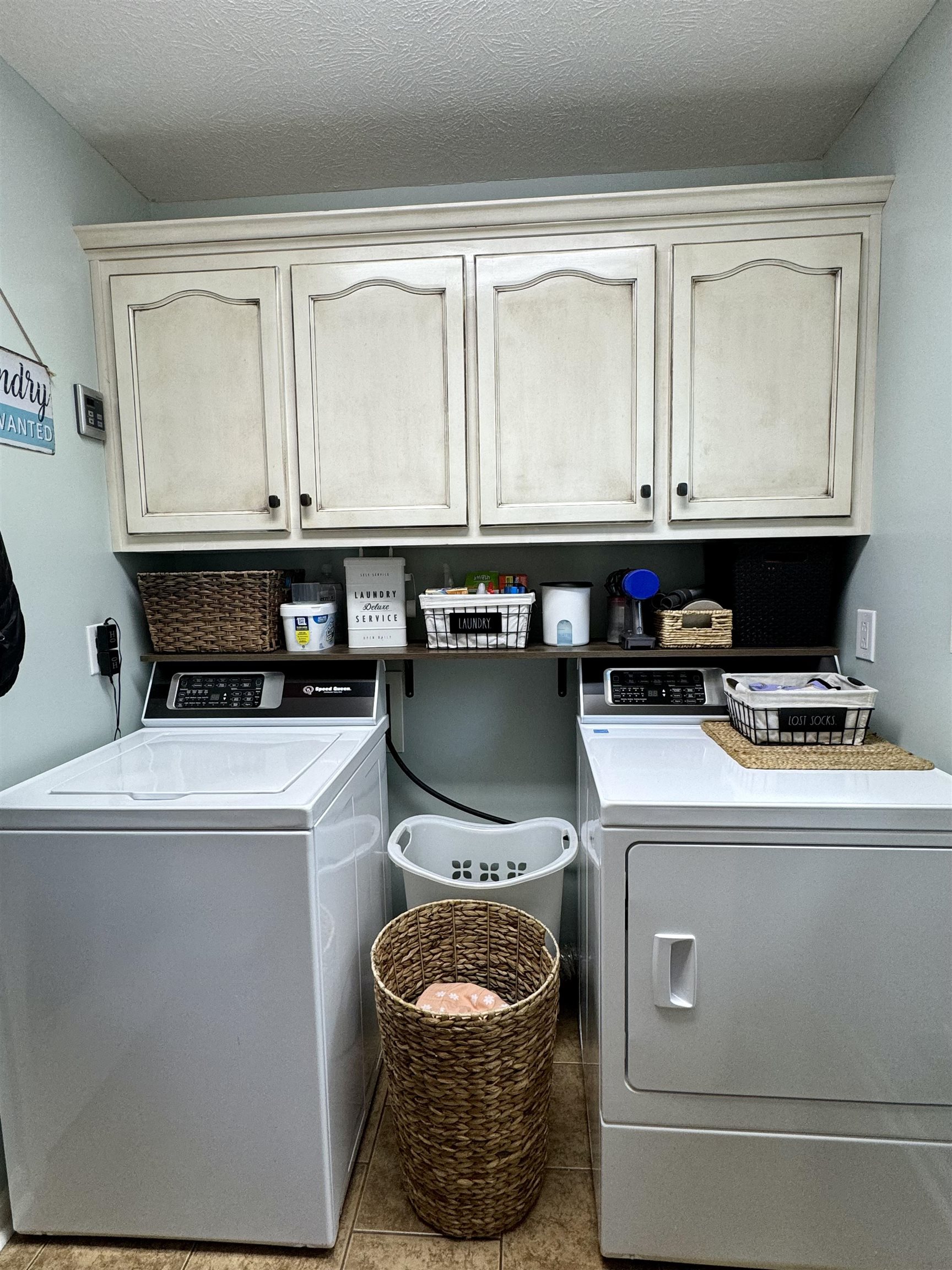 Clothes washing area with a textured ceiling, light tile patterned floors, independent washer and dryer, and cabinets
