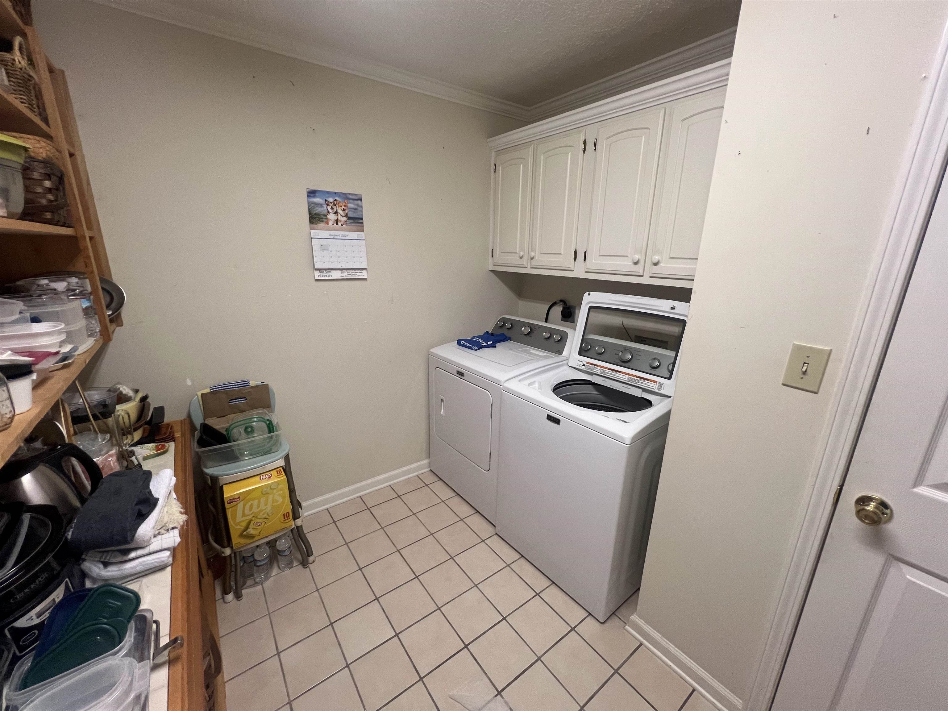 Laundry area featuring light tile patterned floors, ornamental molding, cabinets, and independent washer and dryer