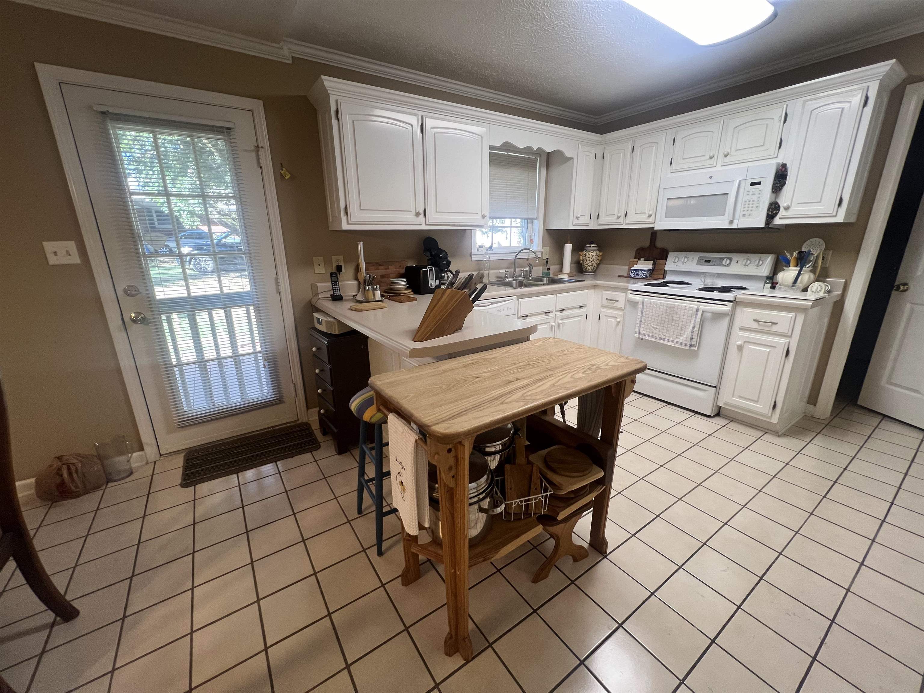 Kitchen with white cabinets, light tile patterned flooring, ornamental molding, and white appliances