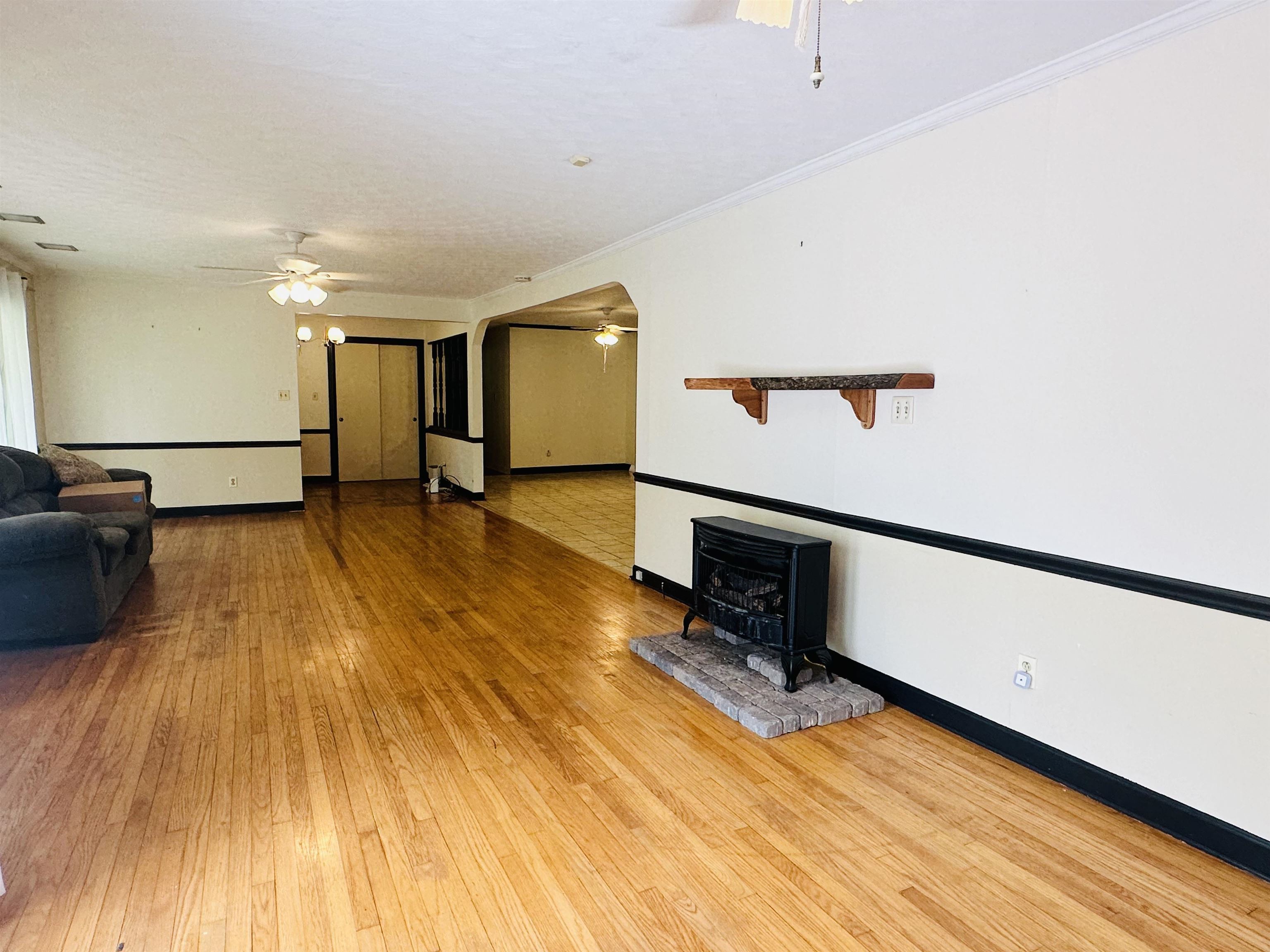 Unfurnished living room with ceiling fan, ornamental molding, a wood stove, wood-type flooring, and a textured ceiling