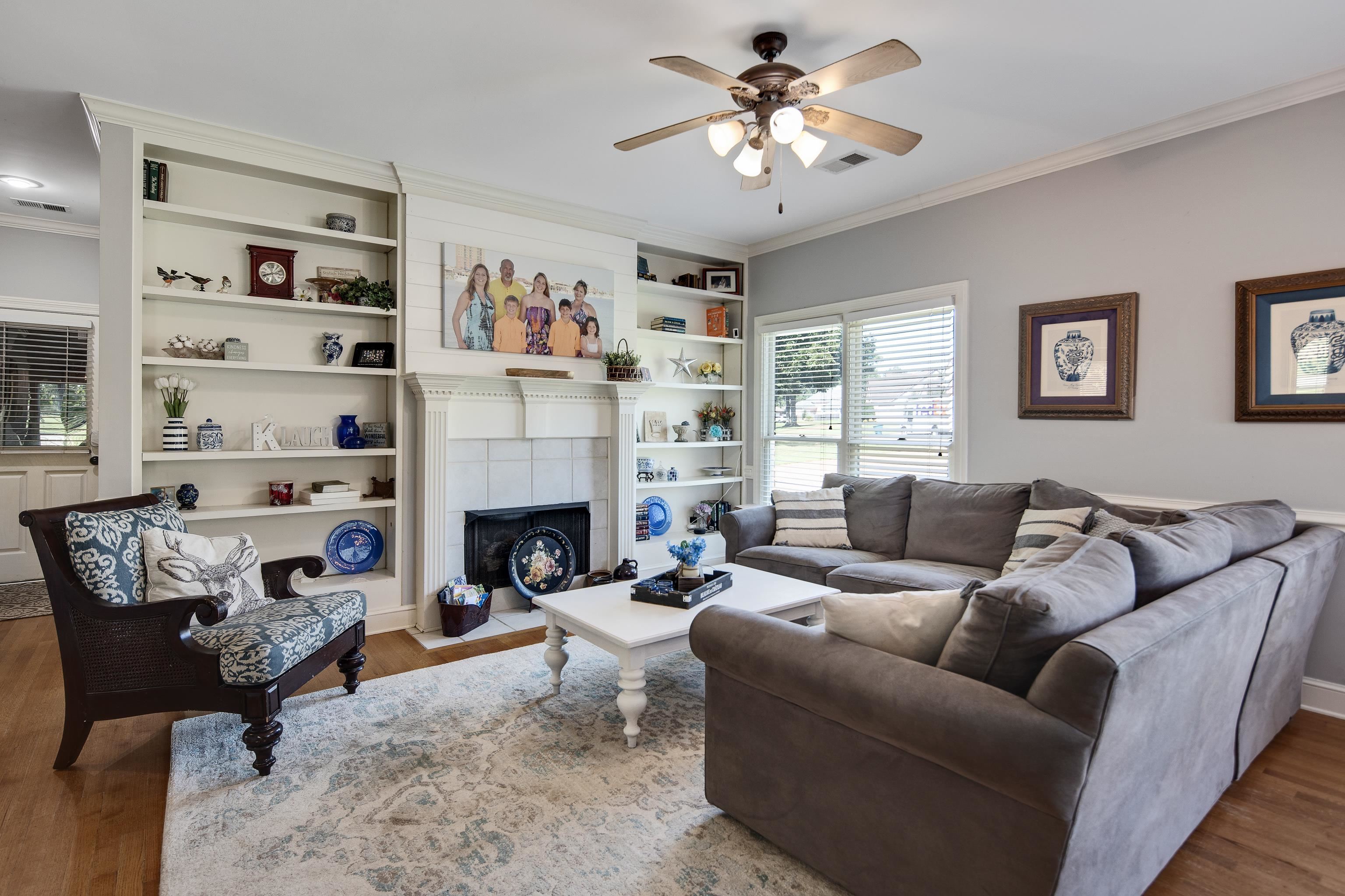 Living room featuring a tile fireplace, crown molding, ceiling fan, built in features, and hardwood / wood-style flooring