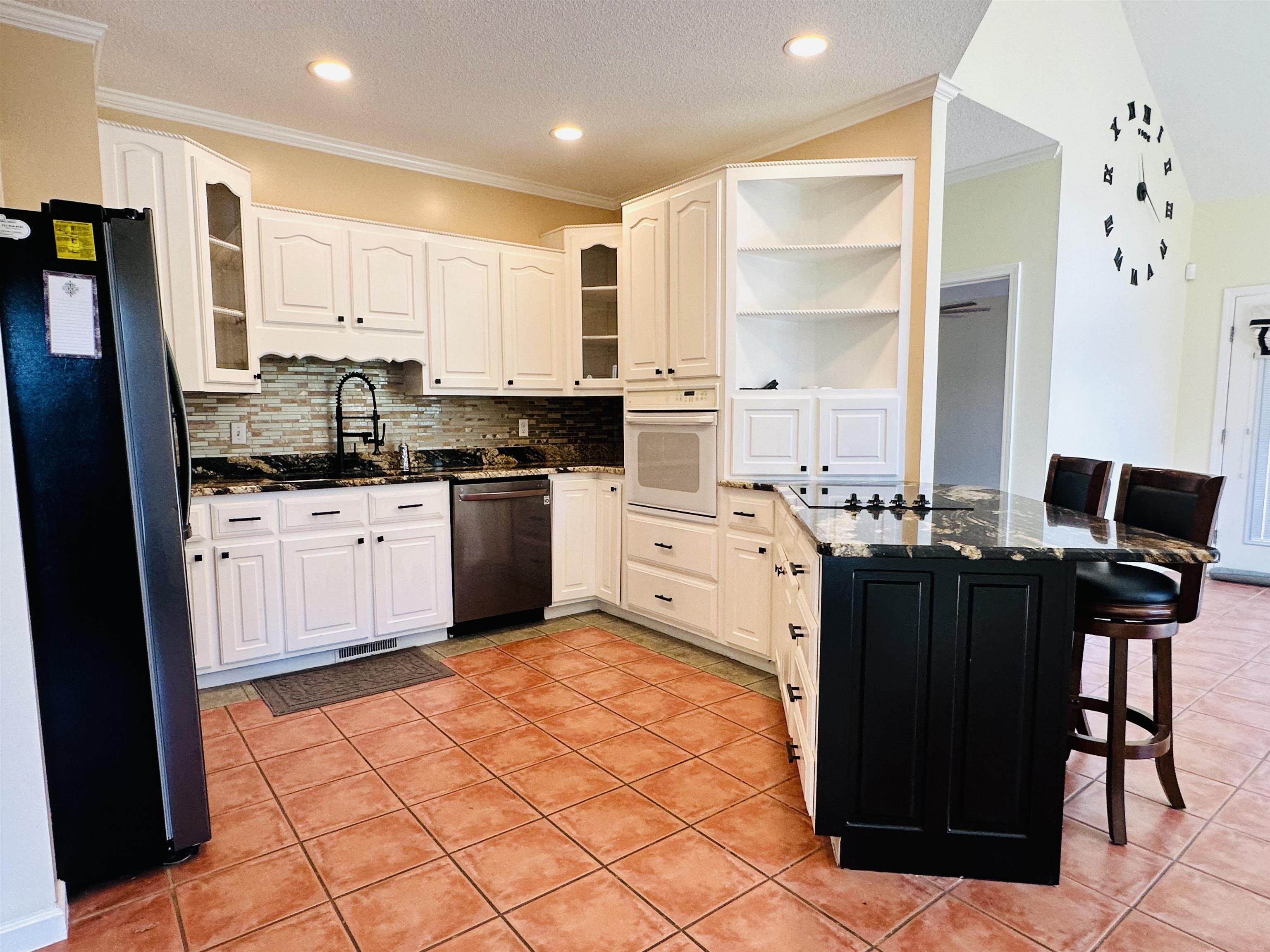 Kitchen featuring a kitchen bar, black appliances, light tile patterned floors, crown molding, and dark stone countertops