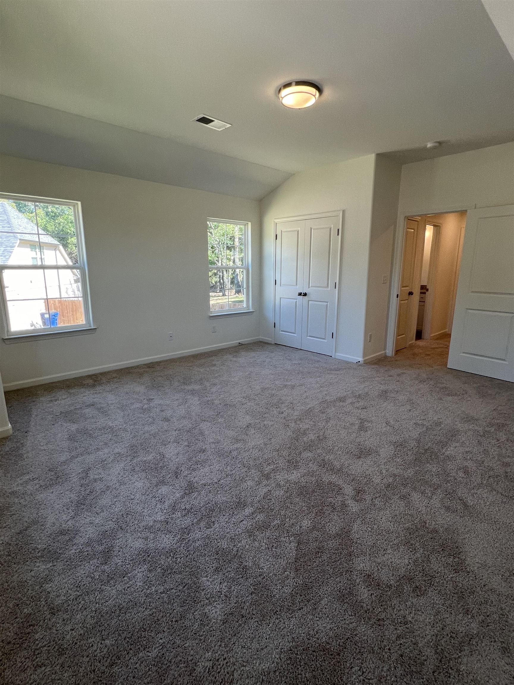 Unfurnished bedroom with vaulted ceiling, carpet flooring, and multiple windows