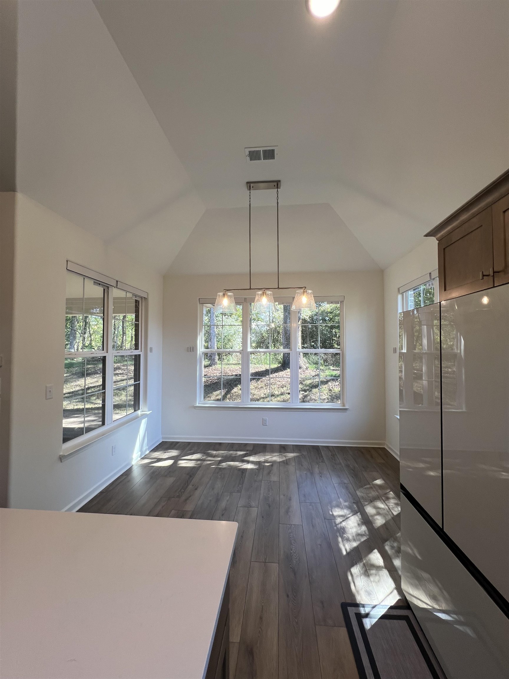 Unfurnished dining area featuring lofted ceiling, an inviting chandelier, and dark wood-type flooring