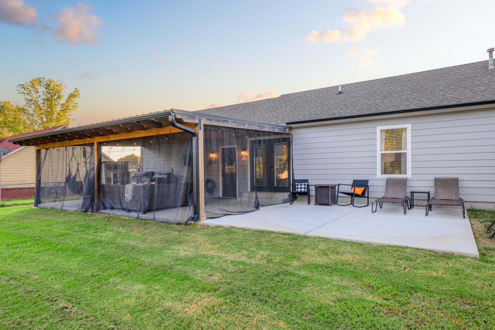 Back house at dusk with a lawn, a patio, and a sunroom