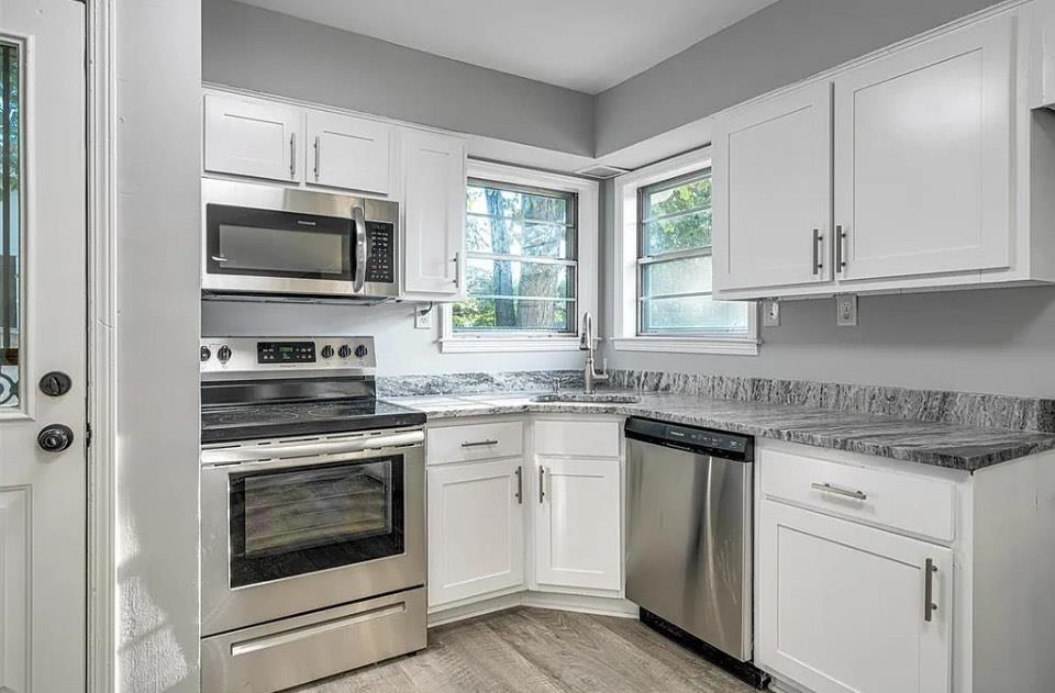 Kitchen with dark stone counters, stainless steel appliances, white cabinetry, and sink