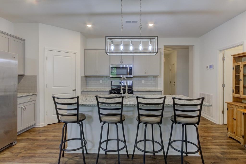 Kitchen featuring light stone countertops, dark wood-type flooring, appliances with stainless steel finishes, and decorative light fixtures