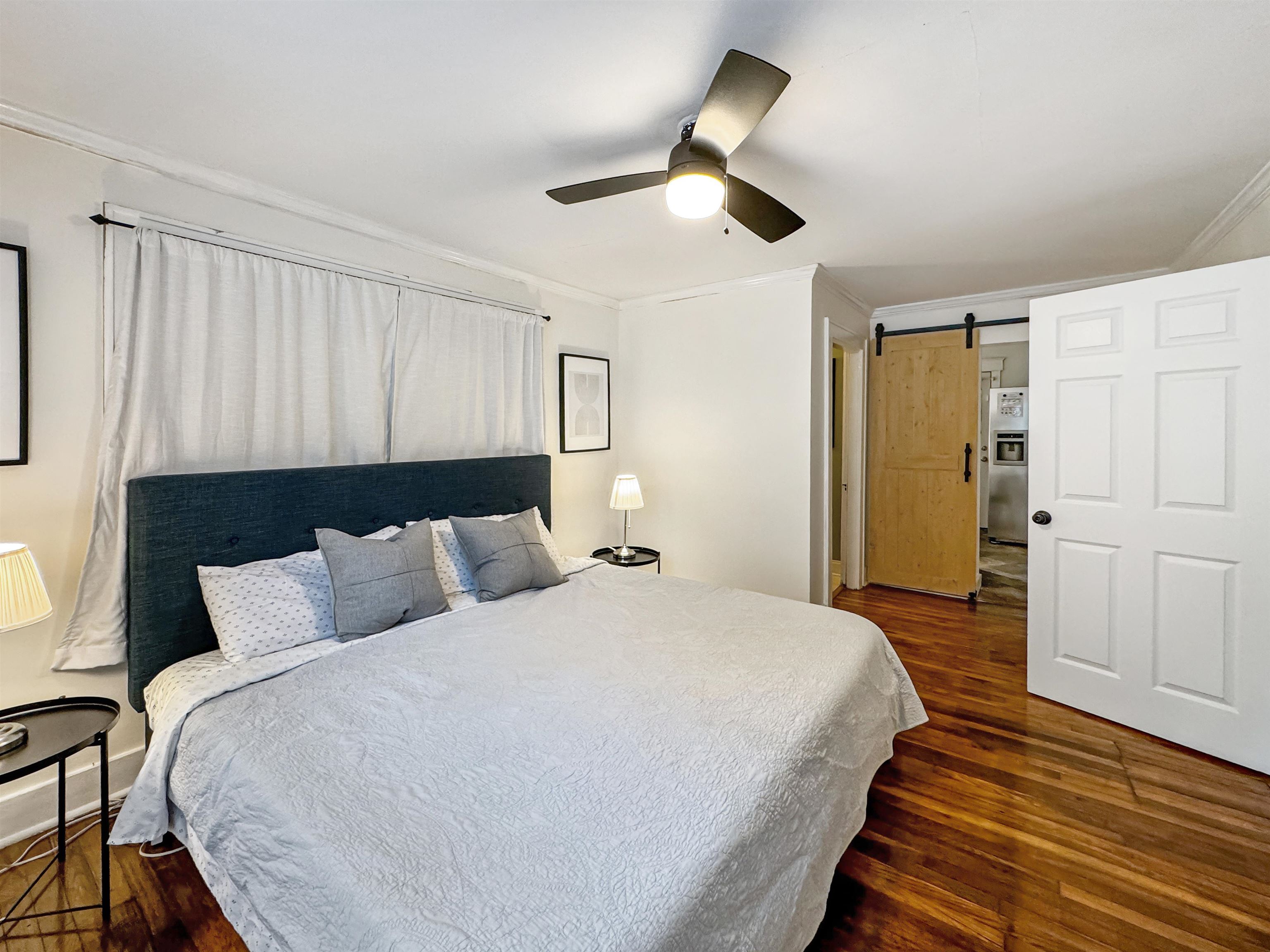 Bedroom with stainless steel refrigerator with ice dispenser, a barn door, dark hardwood / wood-style flooring, ornamental molding, and ceiling fan