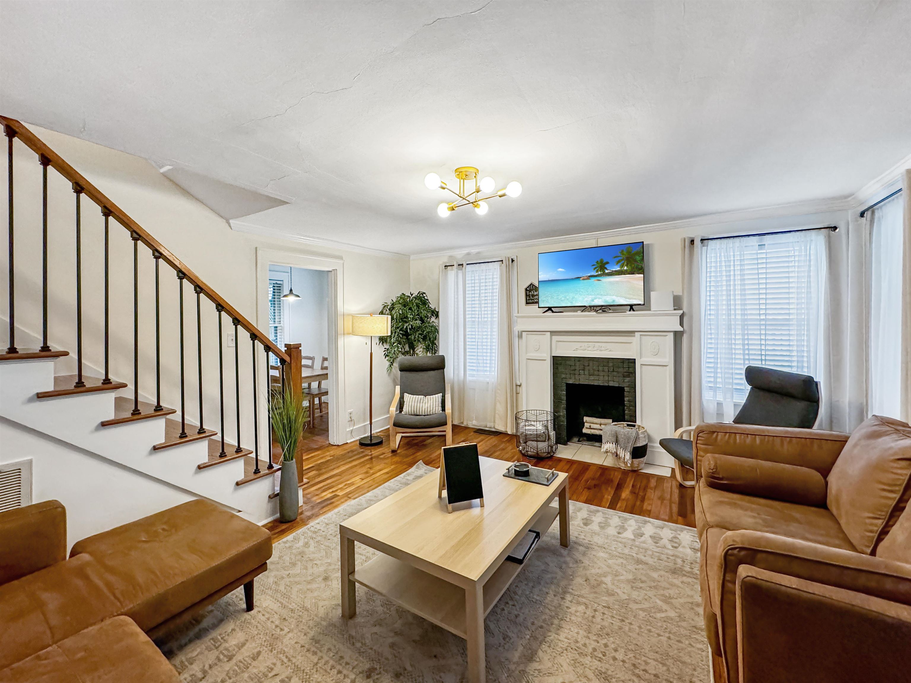 Living room with a notable chandelier, wood-type flooring, a tiled fireplace, and a healthy amount of sunlight
