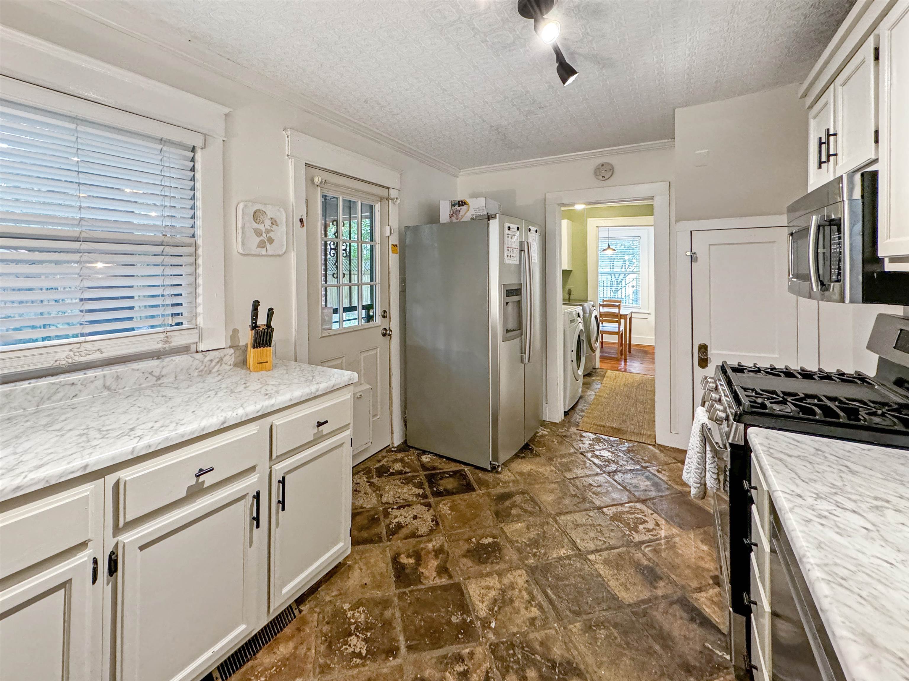 Kitchen featuring white cabinets, appliances with stainless steel finishes, washing machine and clothes dryer, and a wealth of natural light